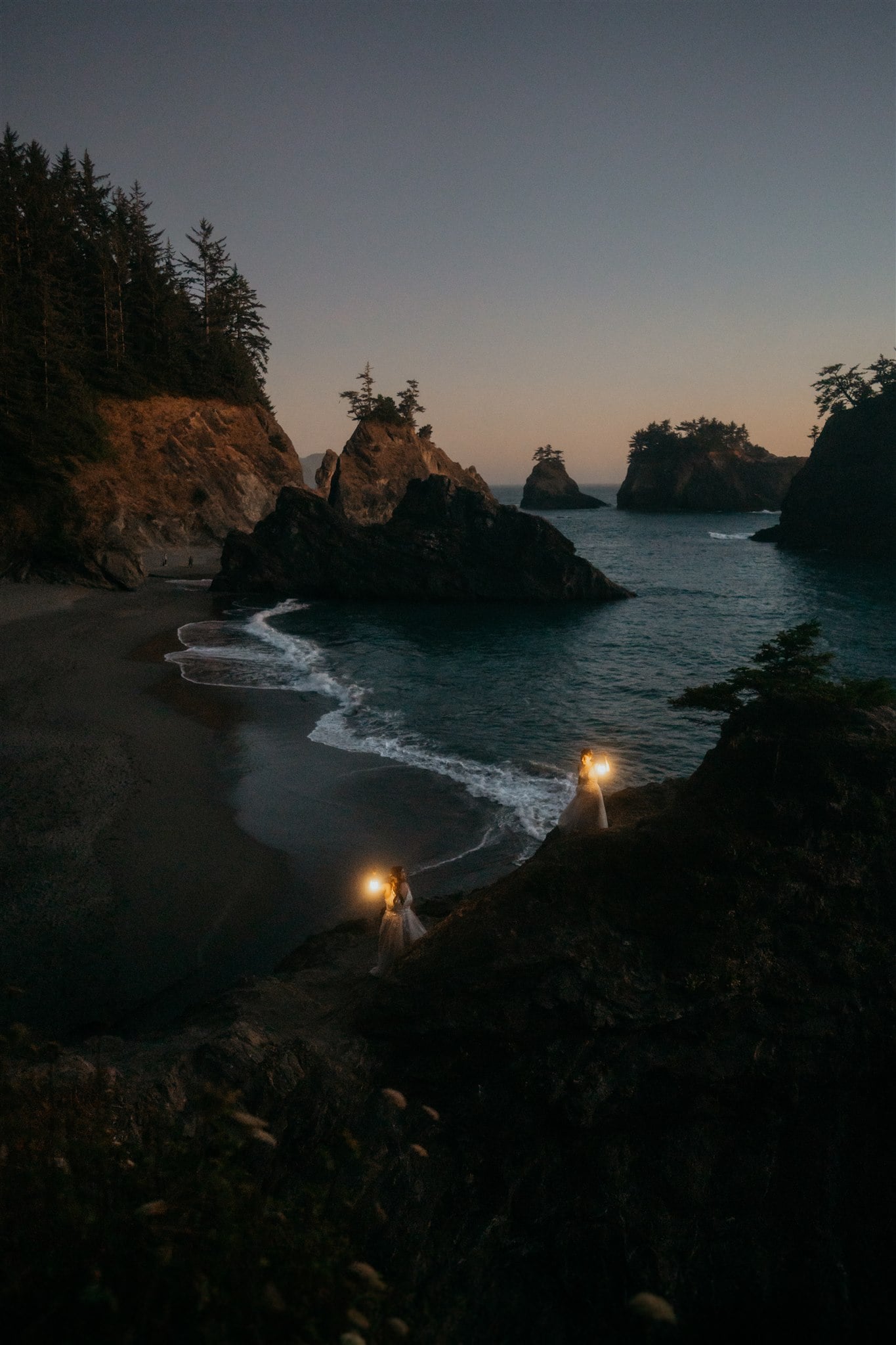 Two brides holding lanterns on the beach during blue hour portraits at elopement at Sunset Beach, Oregon