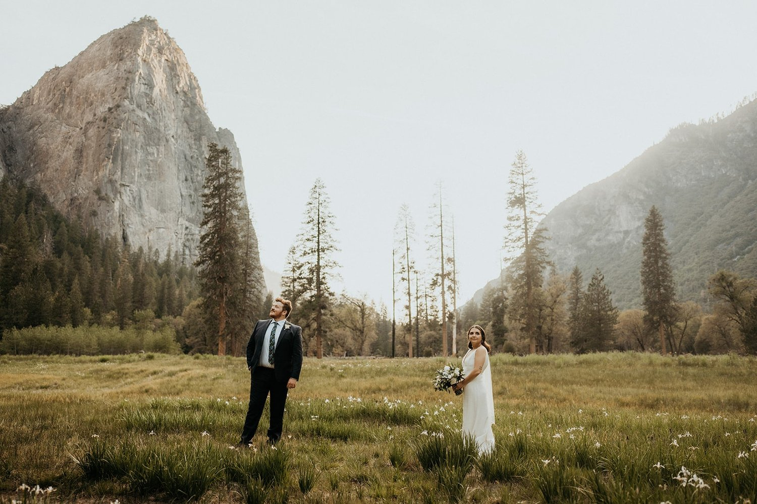 Bride and groom stand in a grassy field during their elopement at El Capitan Meadow in Yosemite.