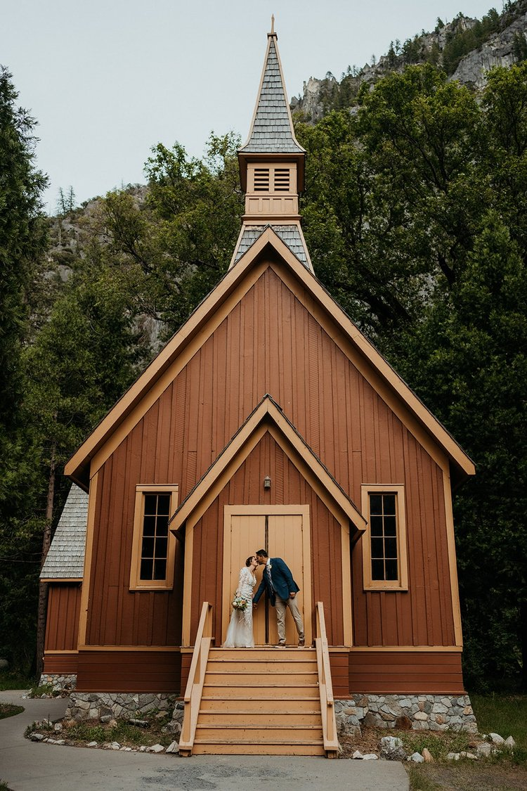 Bride and groom kiss in front of Yosemite chapel.