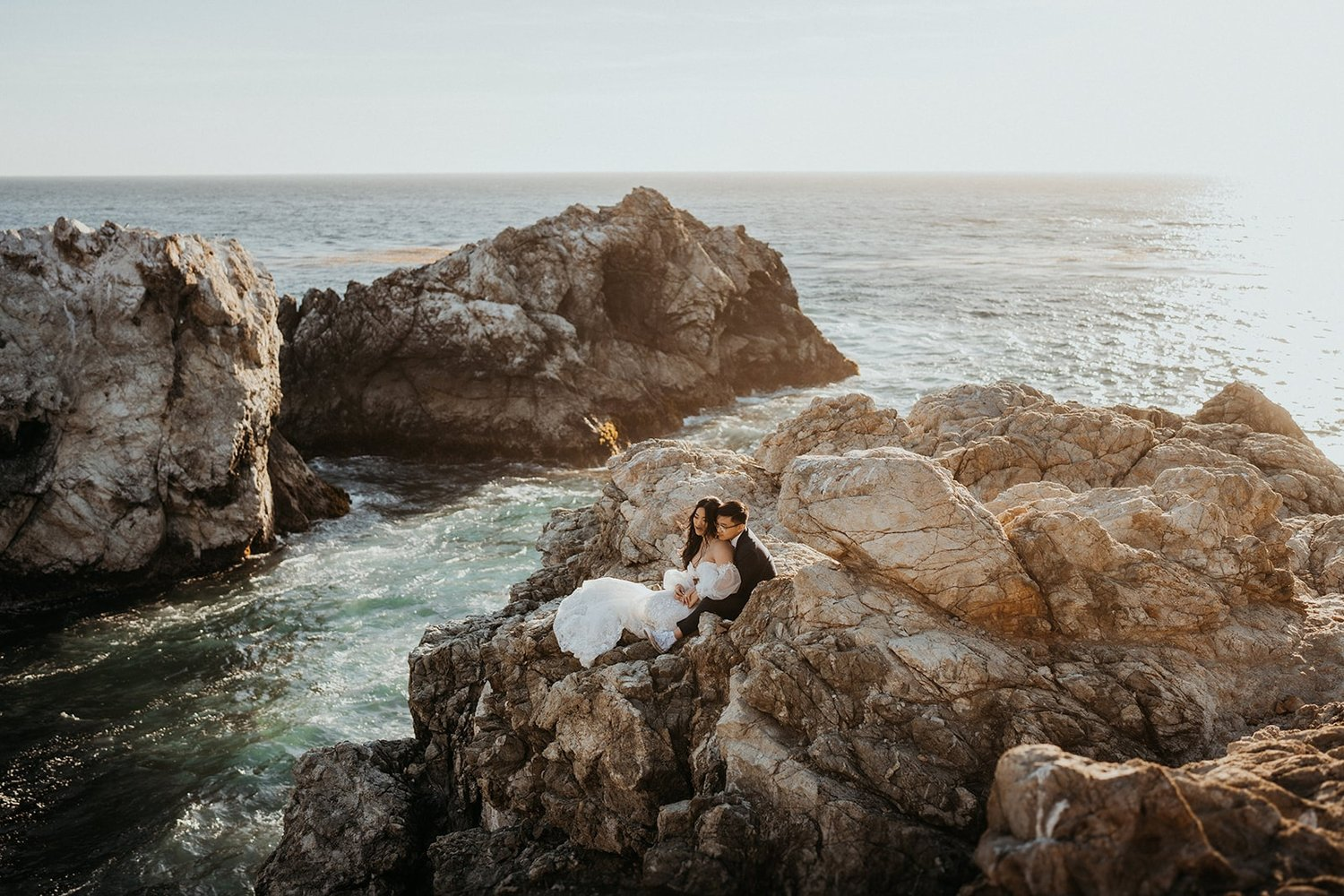 Bride and groom sitting on the cliffs during their Big Sur elopement in California.