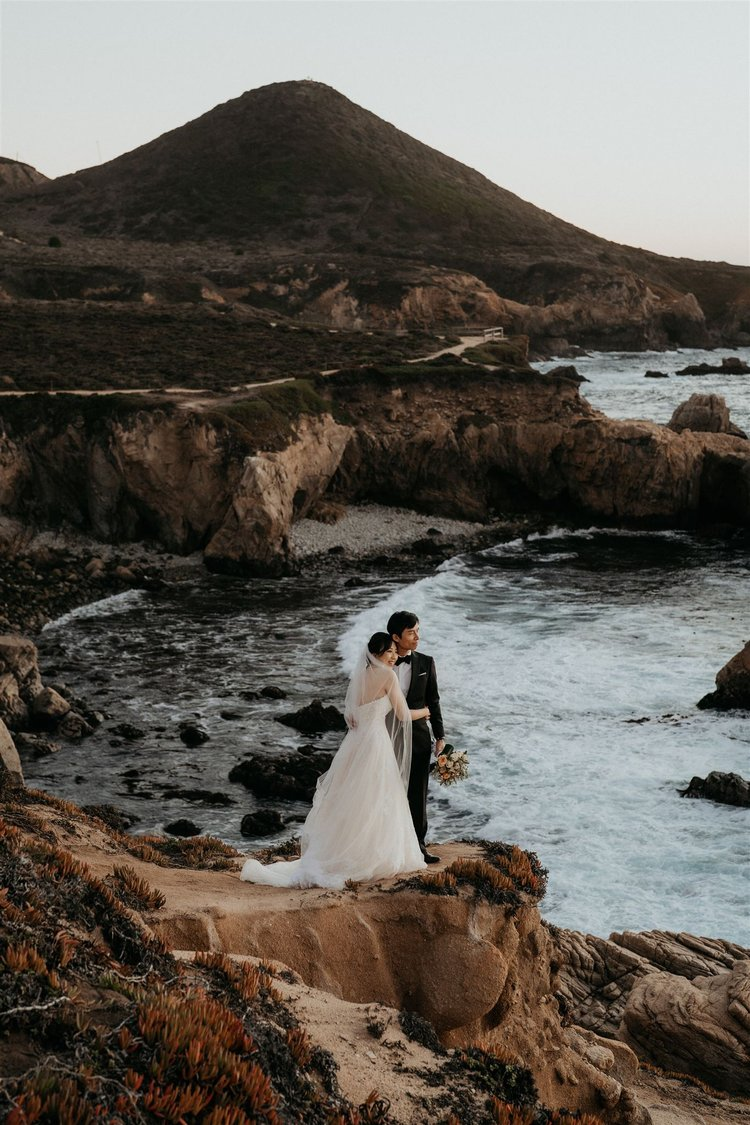 Bride and groom look out at the ocean from a rocky coast during their California elopement in Big Sur.