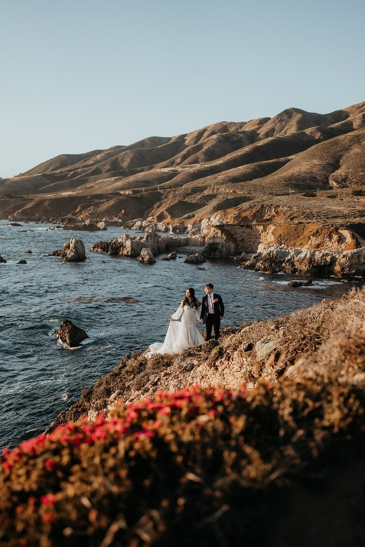 Bride and groom stand on a rocky cliff overlooking the ocean during their Big Sur, California elopement.
