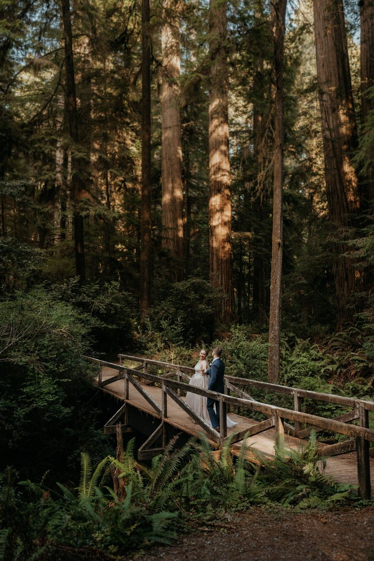 Bride and groom walk across a wood bridge in the forest during their California Redwoods elopement.