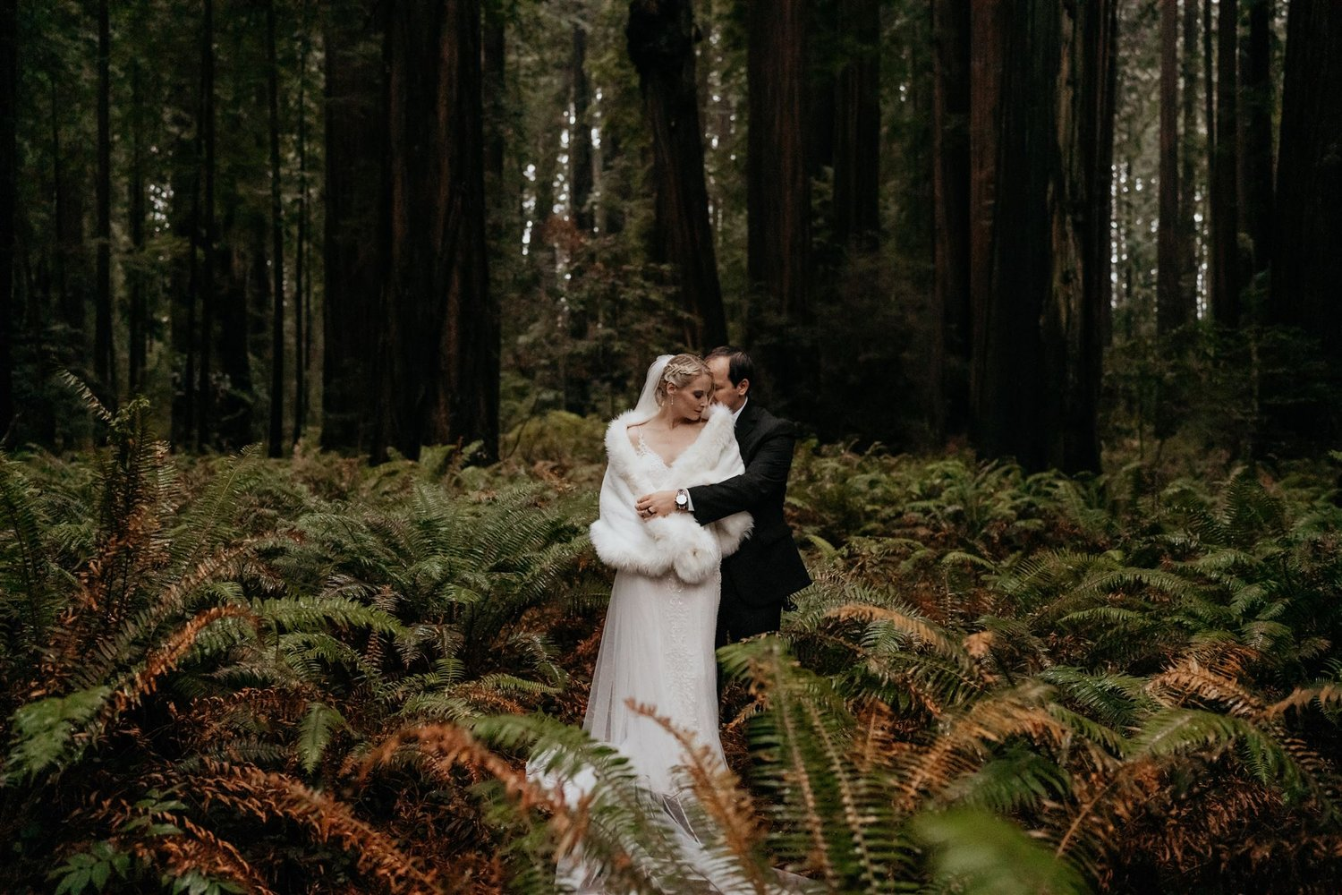 Bride and groom hug in the forest surrounded by ferns during their California Redwoods elopement.