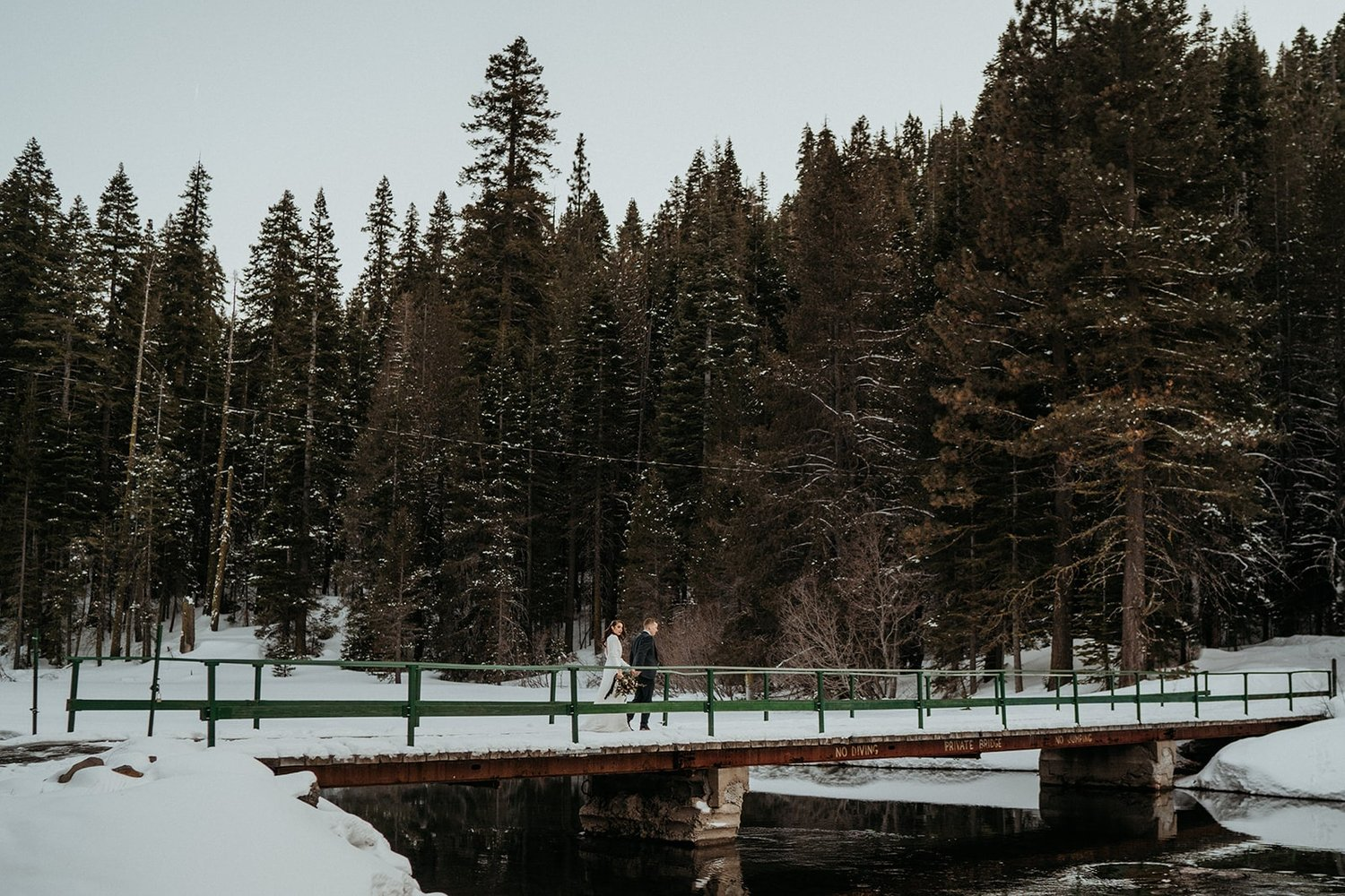 Bride and groom walk across a snowy bridge during their elopement in Lake Tahoe.