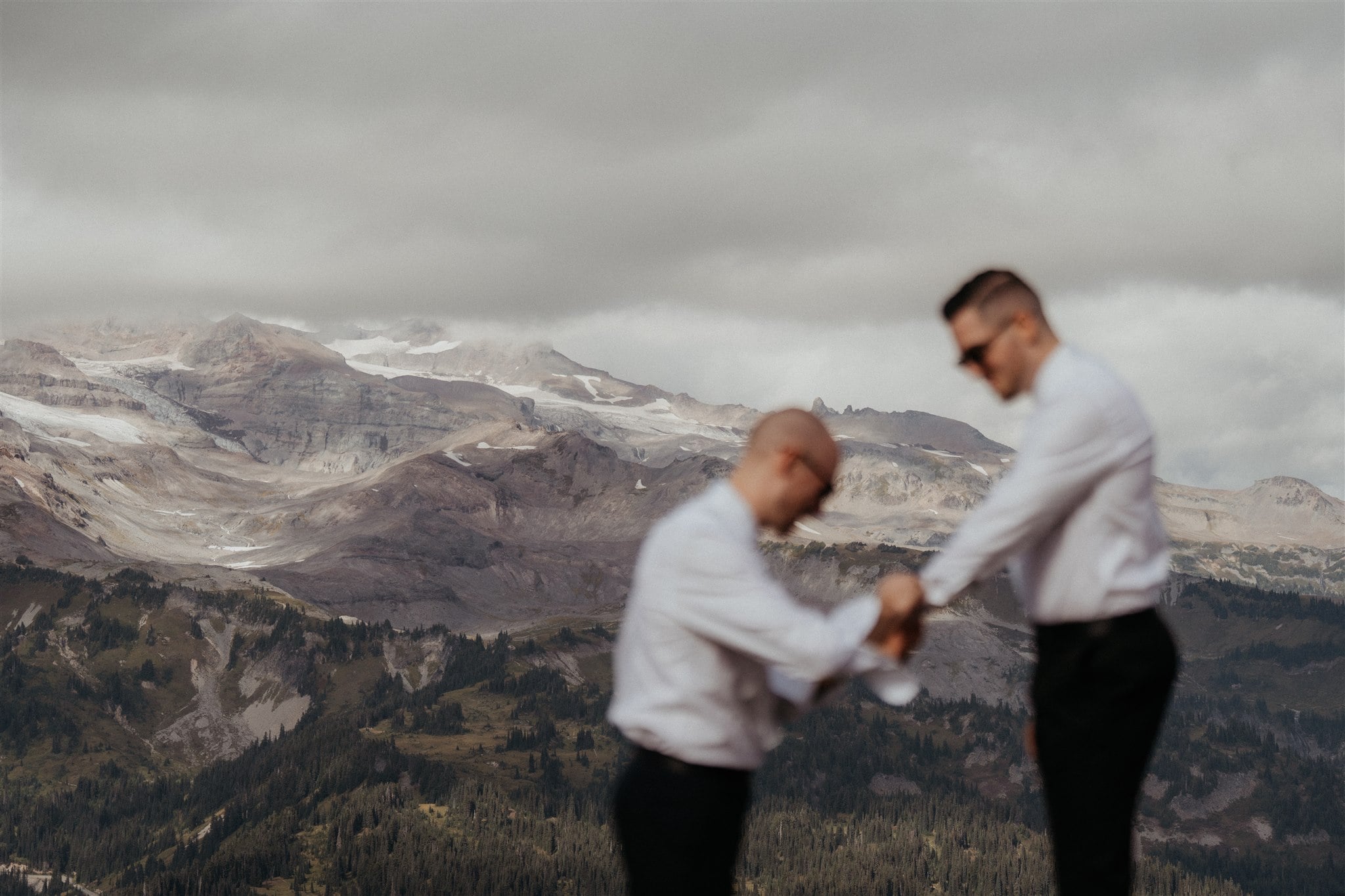 Two grooms help each other getting ready for their elopement on a mountain trail