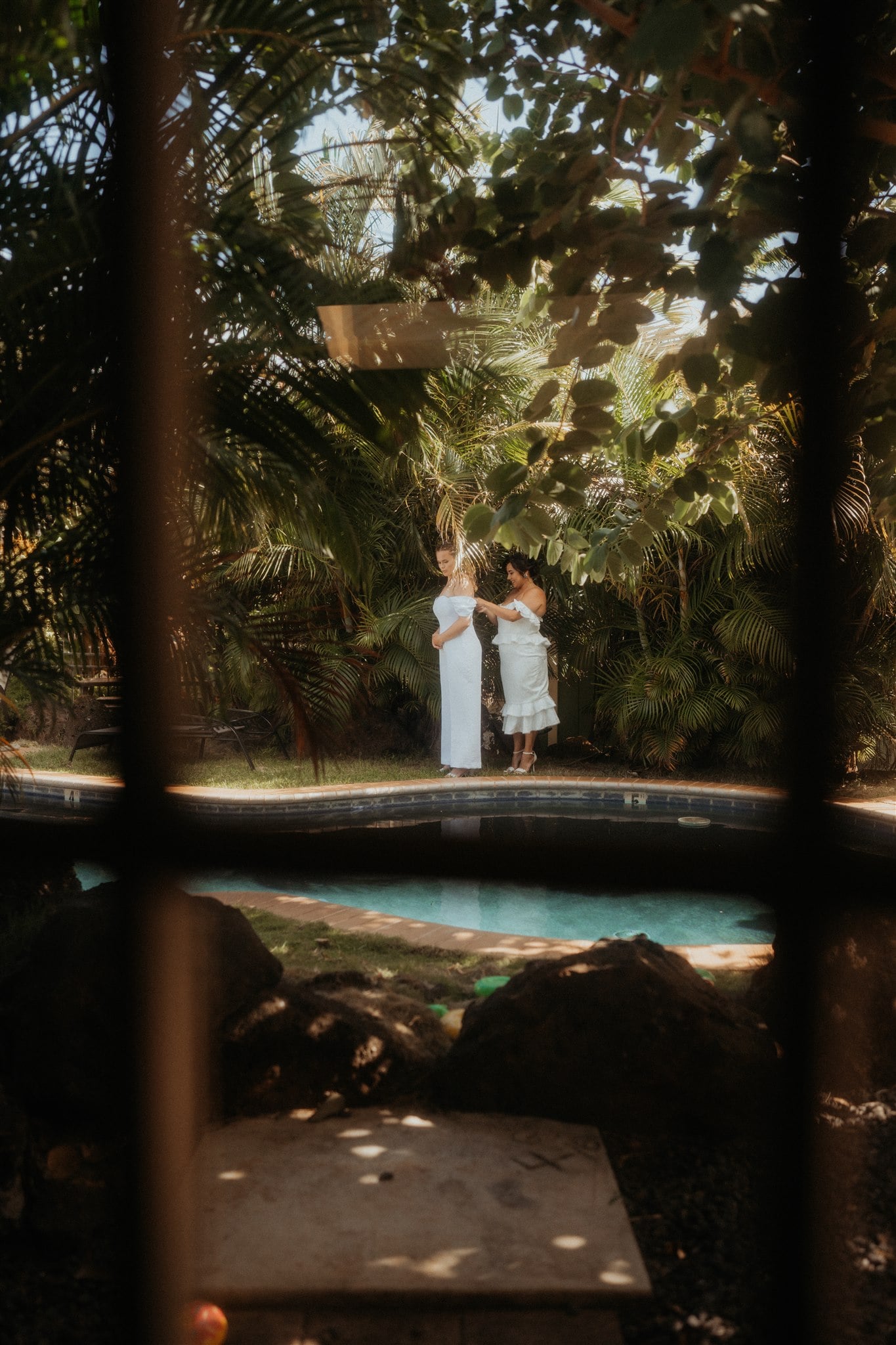 Brides help each other get ready by the pool in their backyard for their Kauai micro wedding.