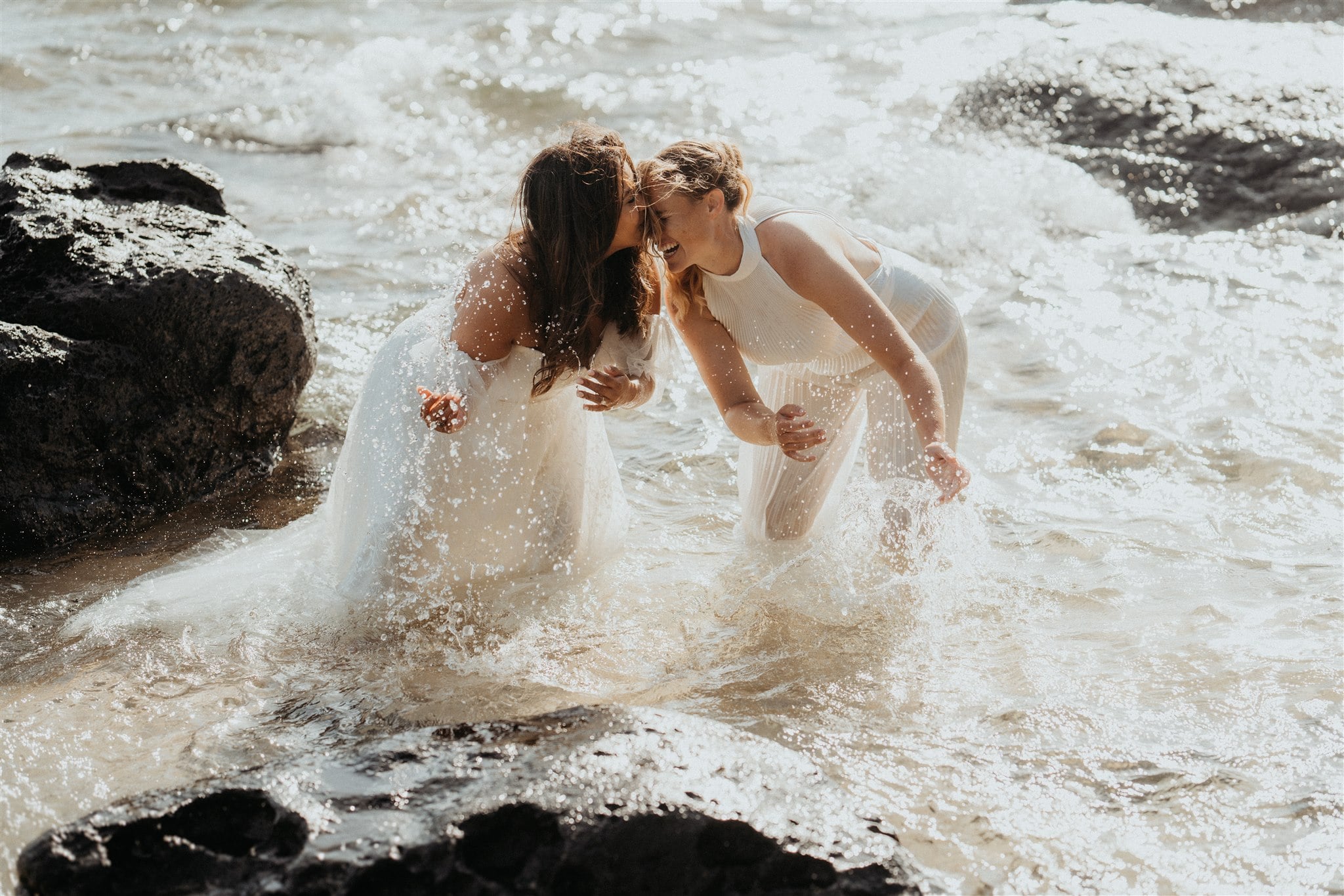Brides laugh and splash in the ocean at Tunnels Beach during their Kauai micro wedding.