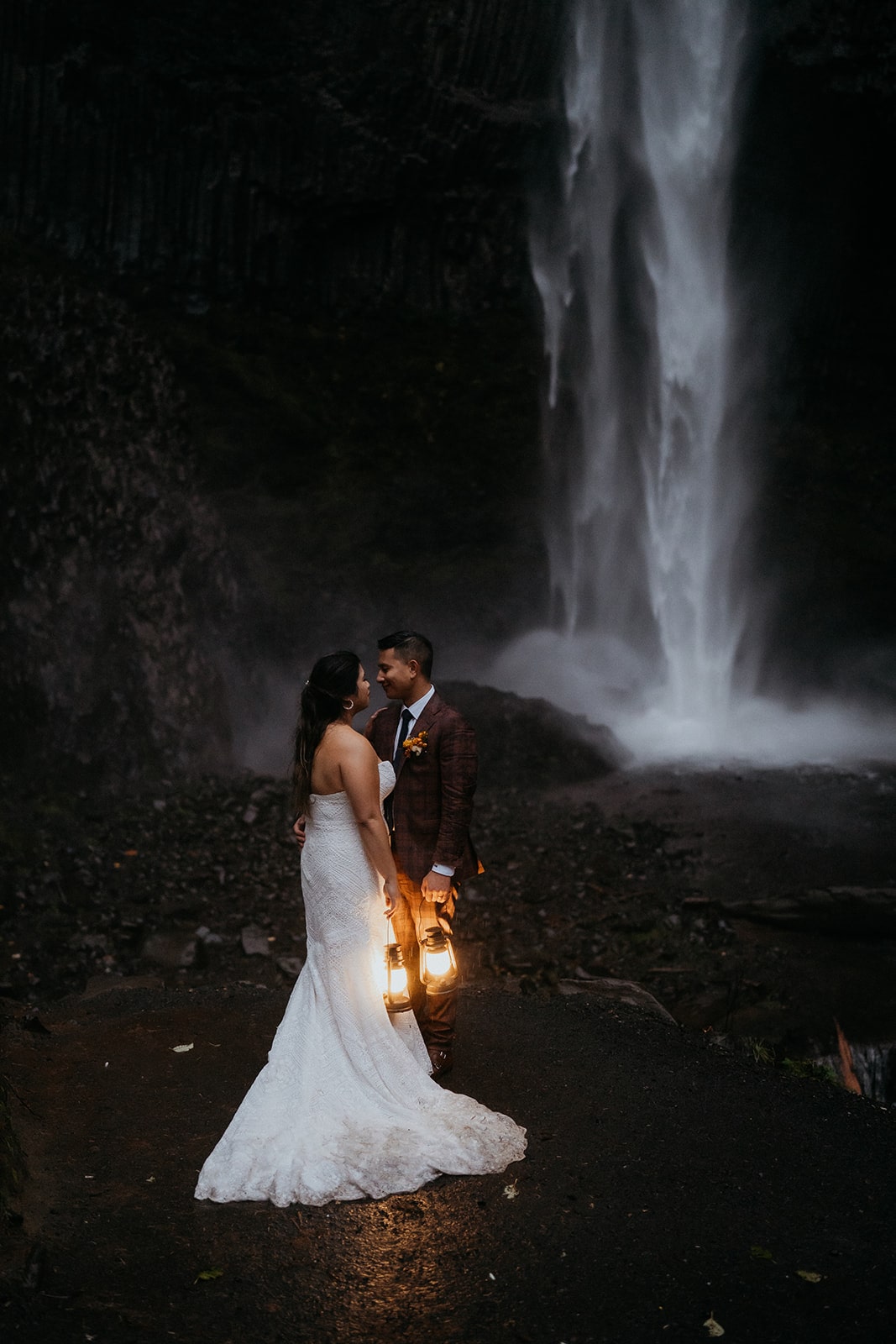 Bride and groom hold lanterns and kiss during their Oregon waterfall elopement.