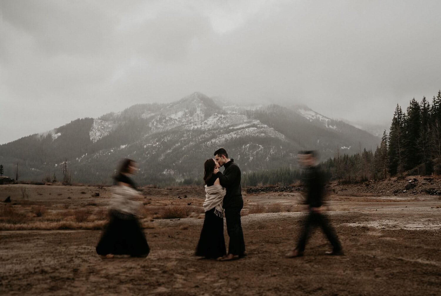 Couple walks towards each other for a kiss in a field surrounded by mountains in Bend, Oregon.