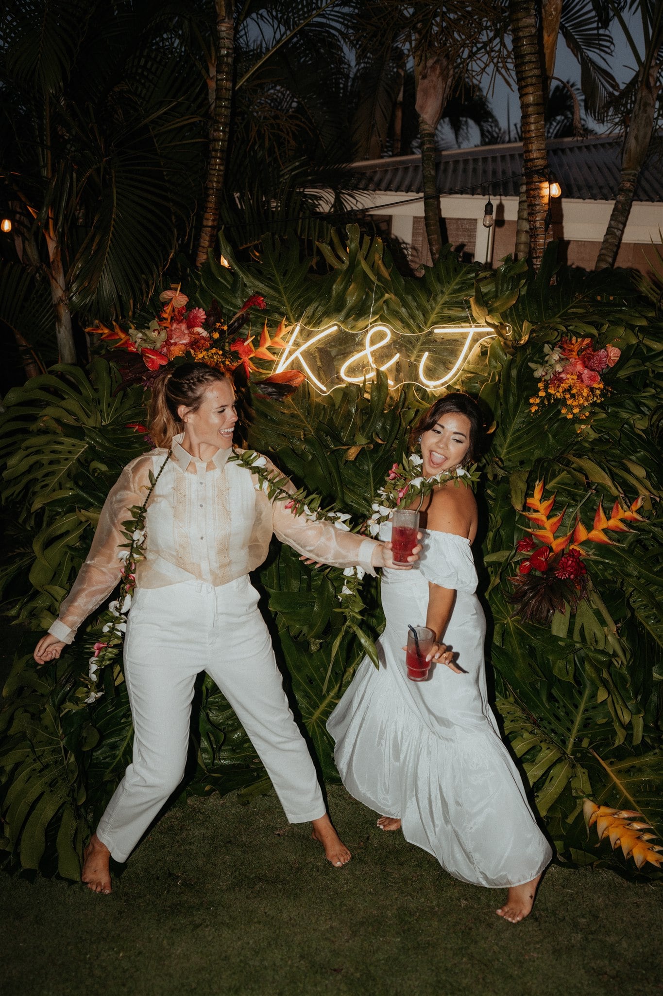 Two brides dance under a K & J neon sign at their Kauai micro wedding reception.