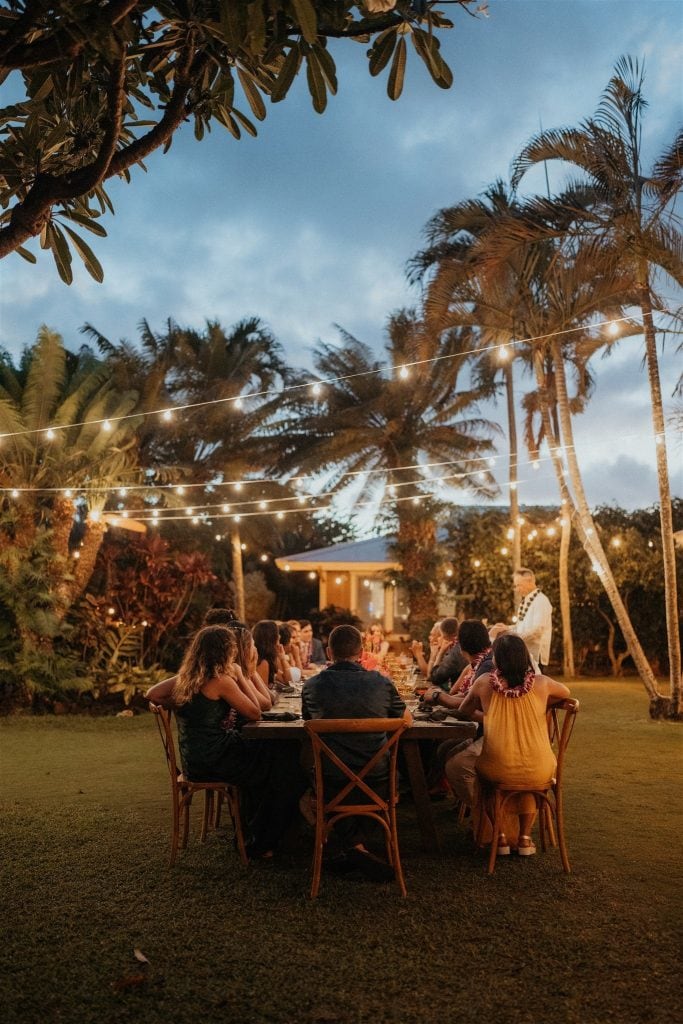 Guests sit around a table under string lights during a micro wedding reception in Kauai.