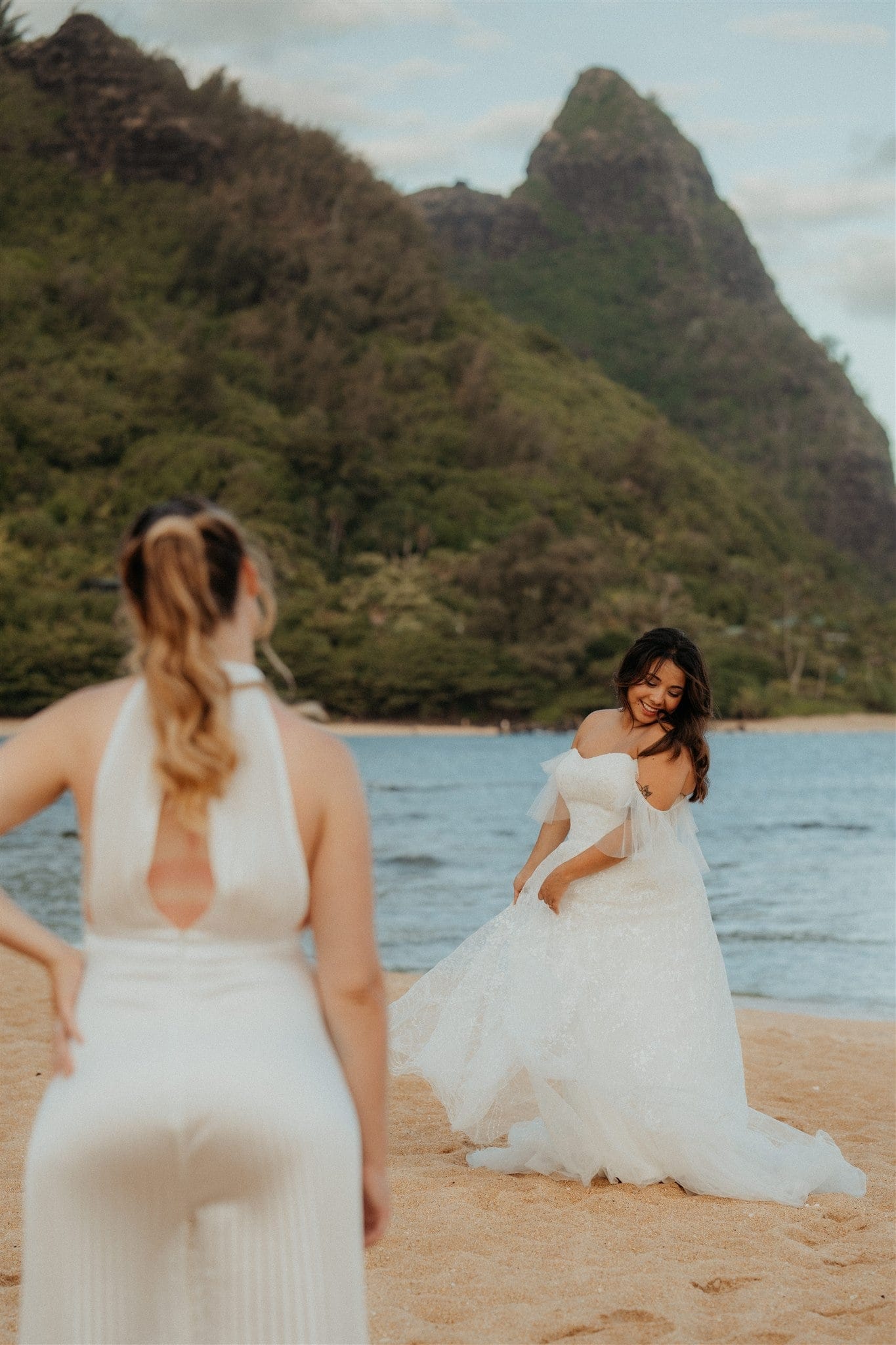 Bride watches as the other bride twirls around in her beach wedding dress.
