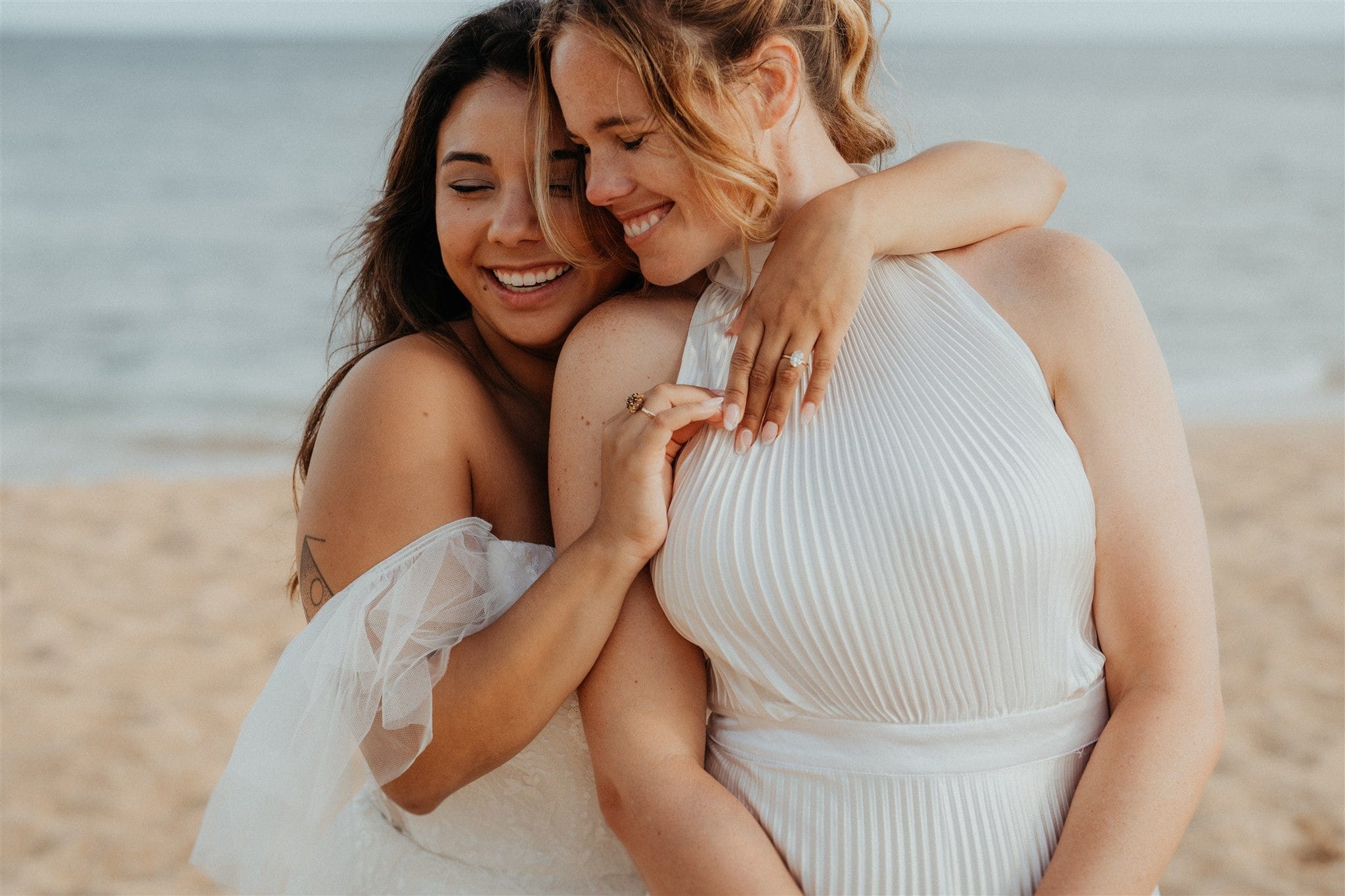 Bride wraps her arms around other bride's neck during their micro wedding photos at Tunnels Beach.