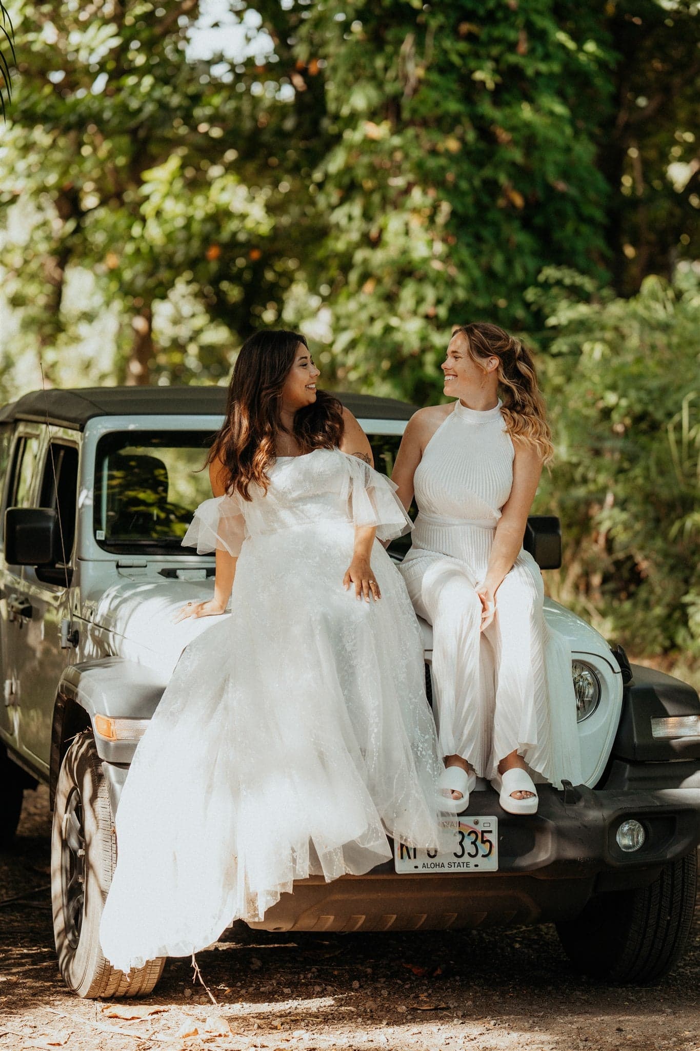 Brides sit on the hood of their Jeep after their adventure photos at Tunnels Beach in Kauai.