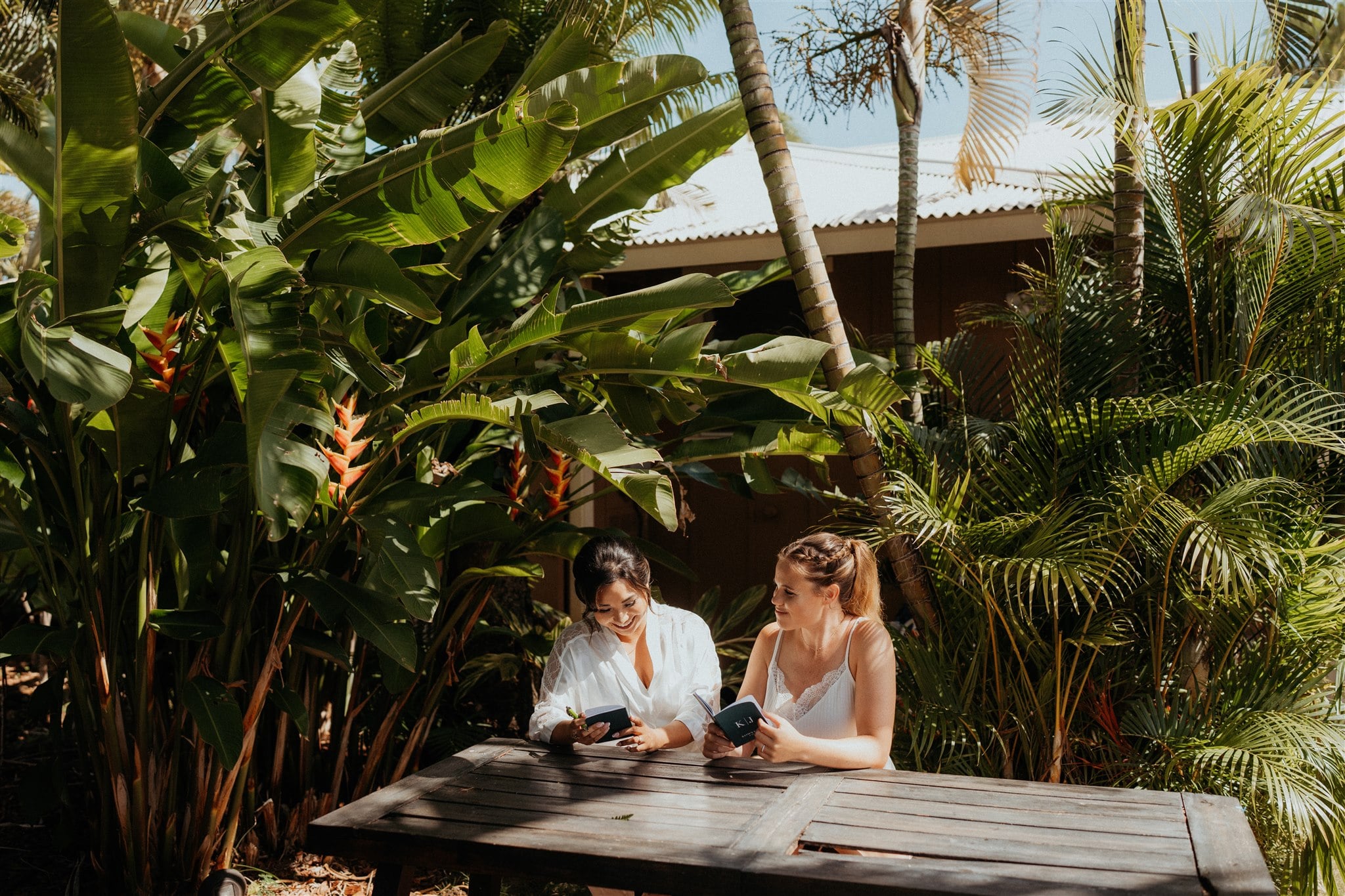 Two brides sit at a picnic table writing their personal vows before their micro wedding in Kauai.