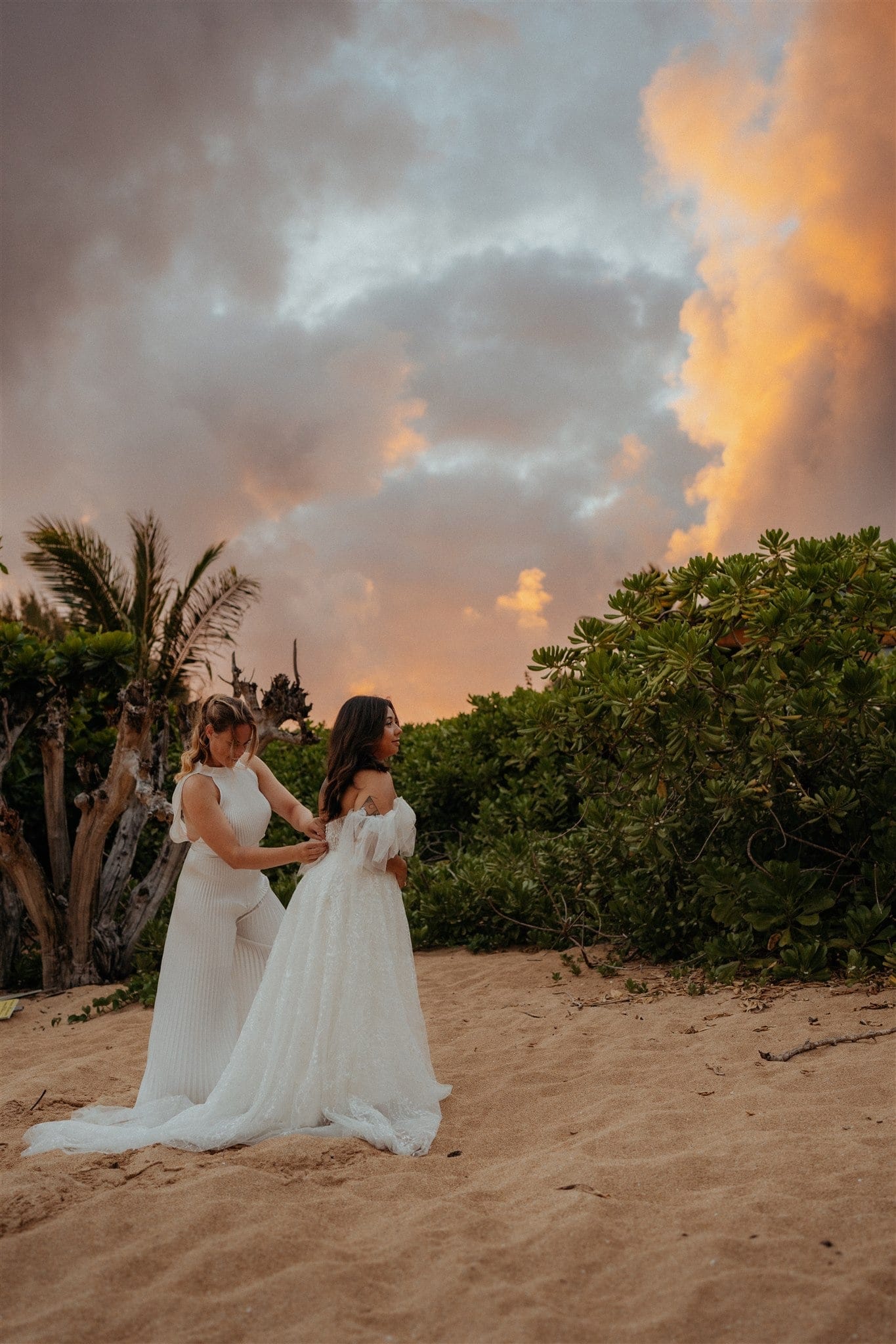 Bride helps zip other bride into her beach wedding dress during their micro wedding in Kauai.