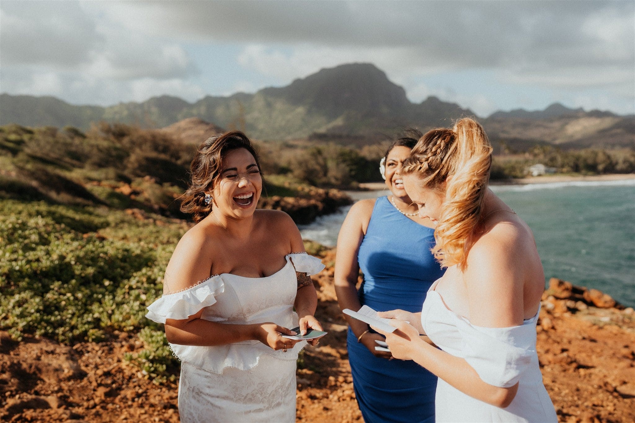 Brides laugh while exchanging personal vows at their Kauai micro wedding on the cliffs.
