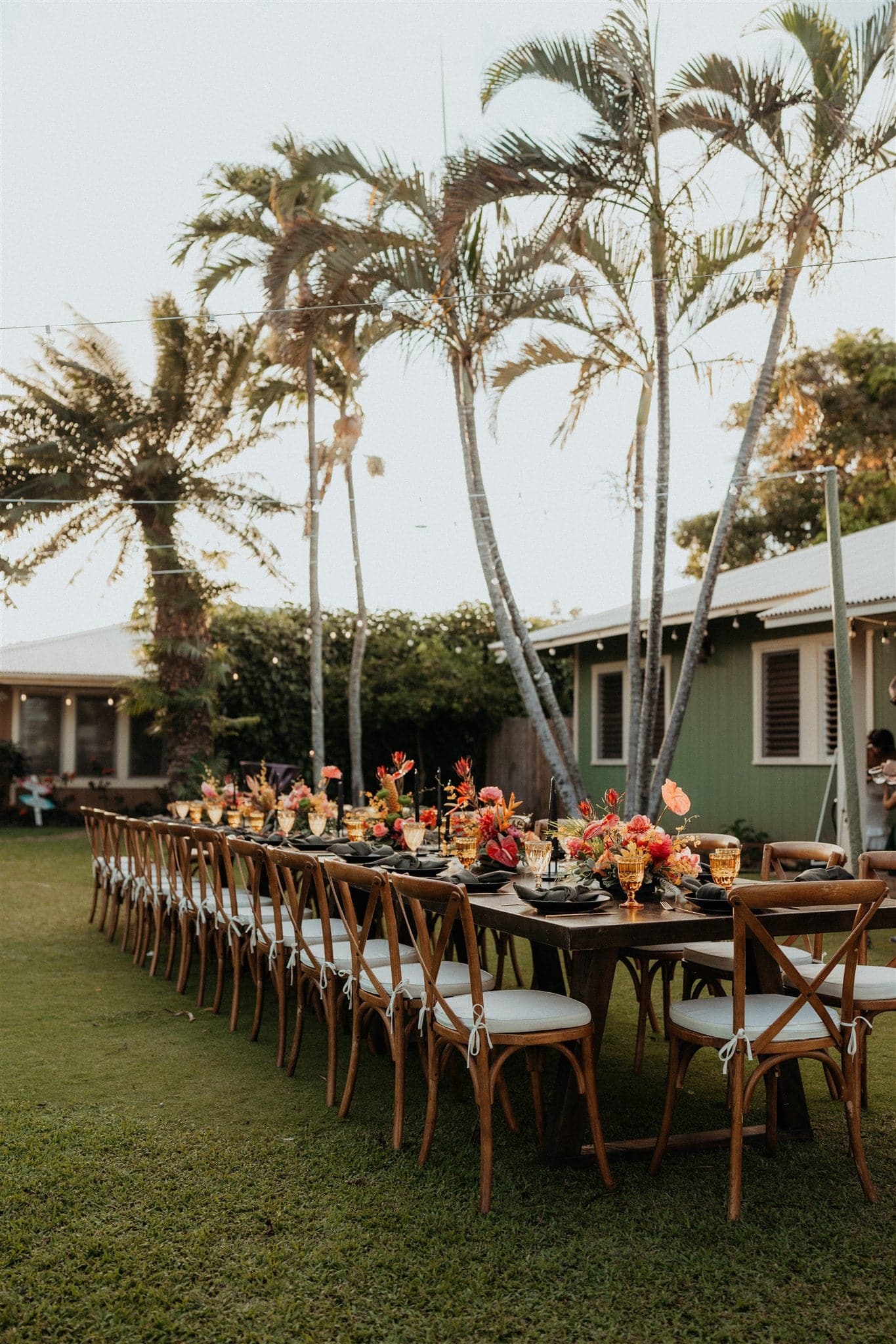 Bright pink and orange tropical florals line a Kauai micro wedding dinner reception table in the backyard of an Airbnb.