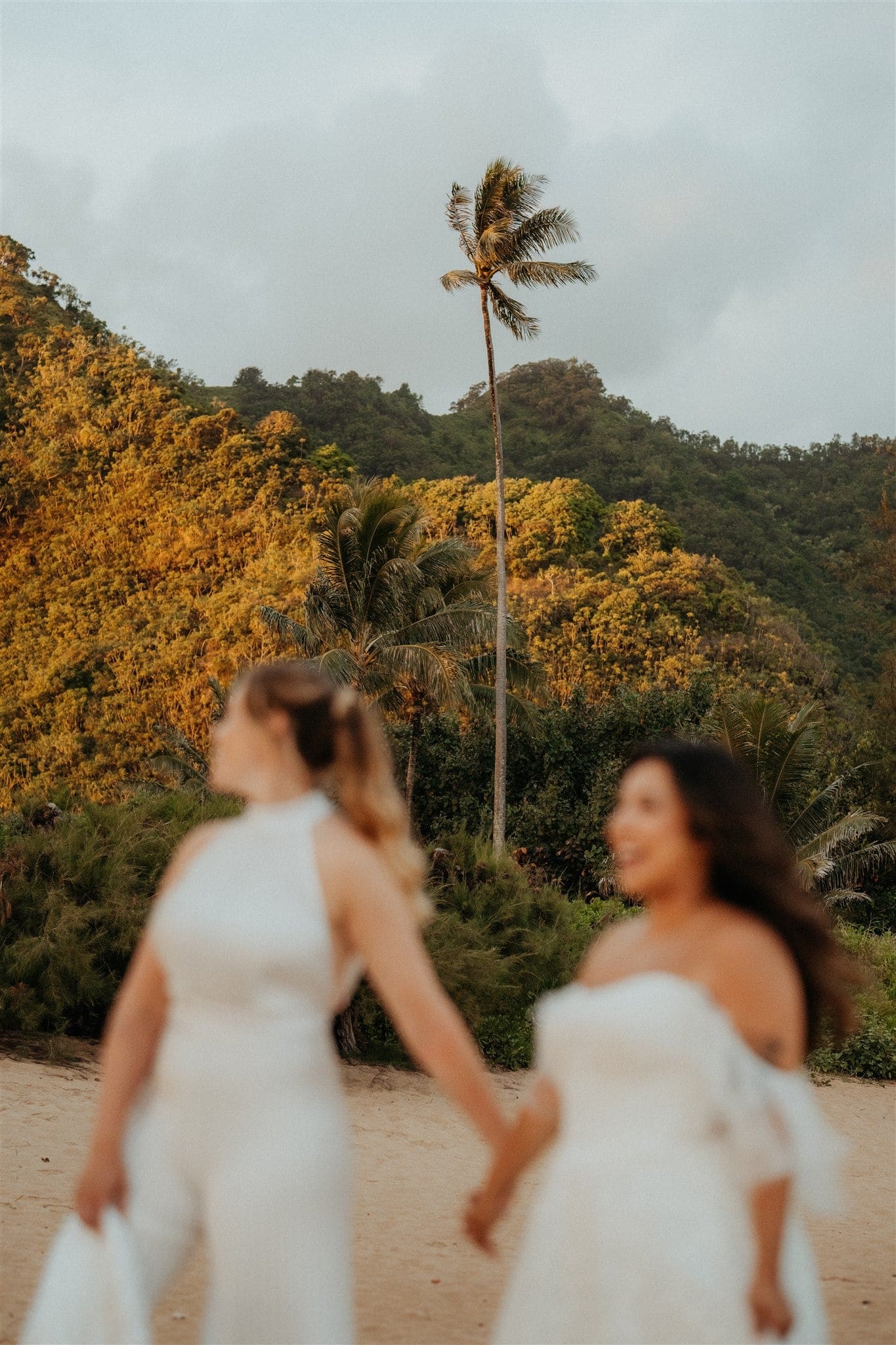 Brides hold hands on Tunnels Beach during their adventure session in Kauai.