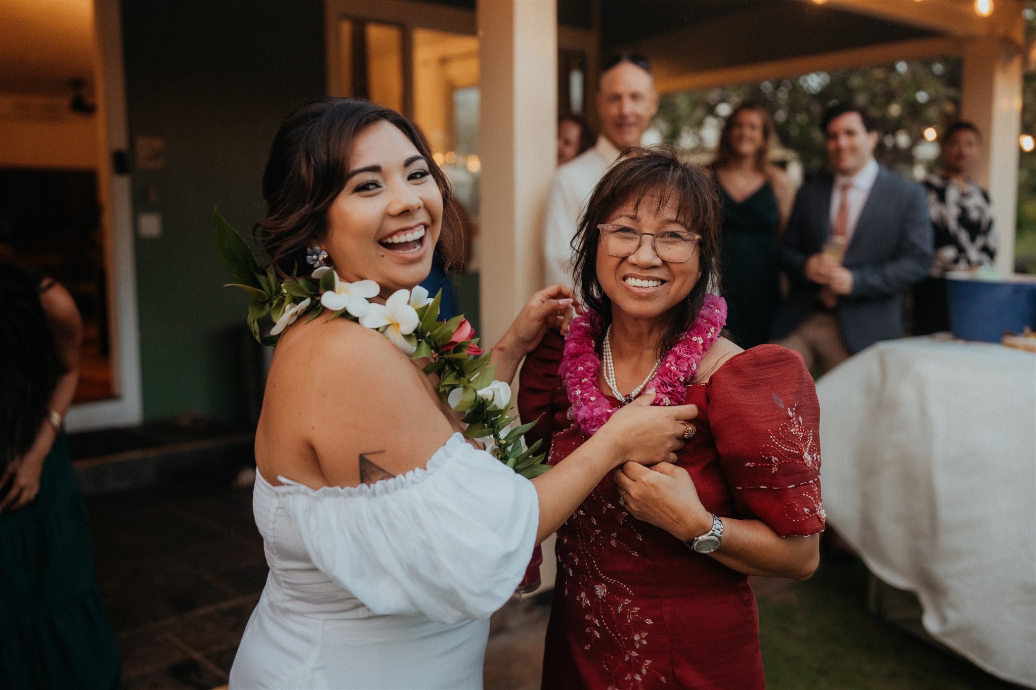 Bride smiles as she puts a lei around a guests shoulders at her Kauai micro wedding reception.