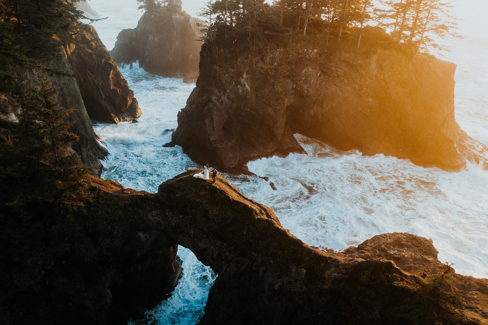 Two brides hold hands while walking across Natural Bridges during their Oregon Coast elopement.