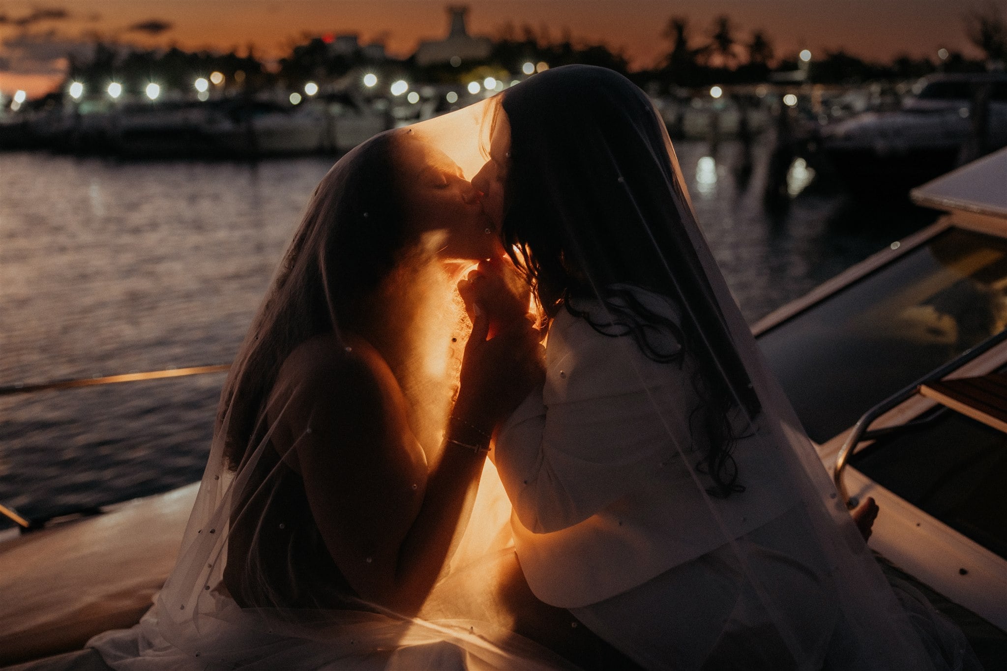 Brides kiss on the deck of a boat after sunset during their Mexico elopement in Cancun.