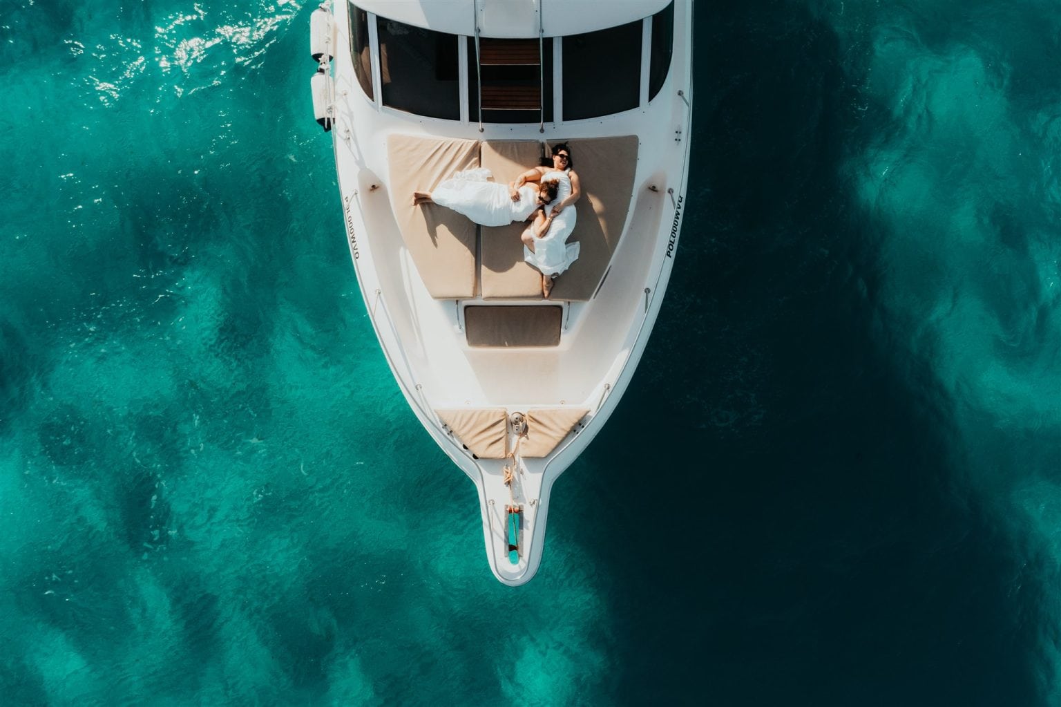 Brides lay on the deck of a boat surrounded by clear blue water during their Cancun elopement.