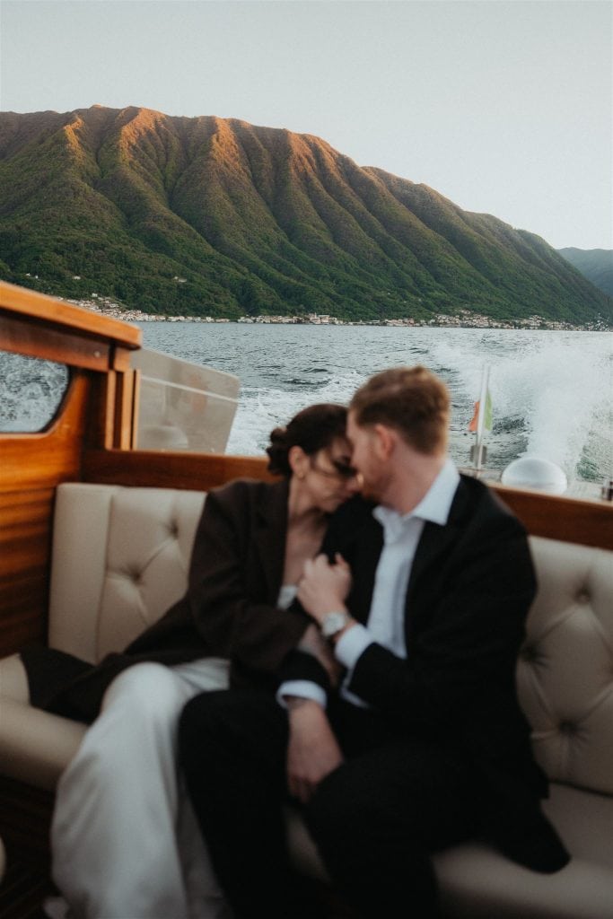 Bride and groom rest their foreheads against each other while riding a boat around Lake Como at sunset.