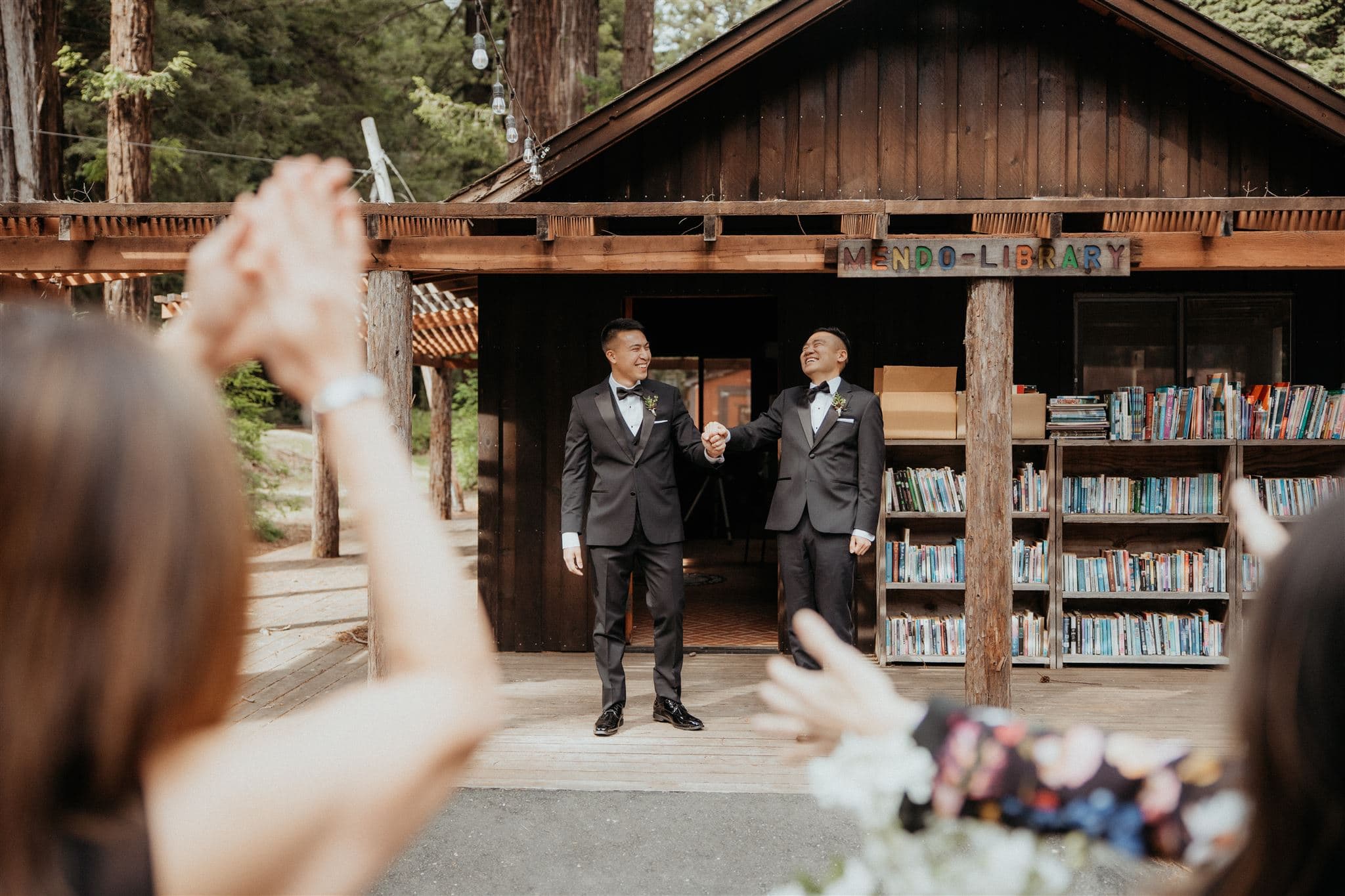 Two grooms hold hands while guests clap during a wedding weekend in Mendocino, California.