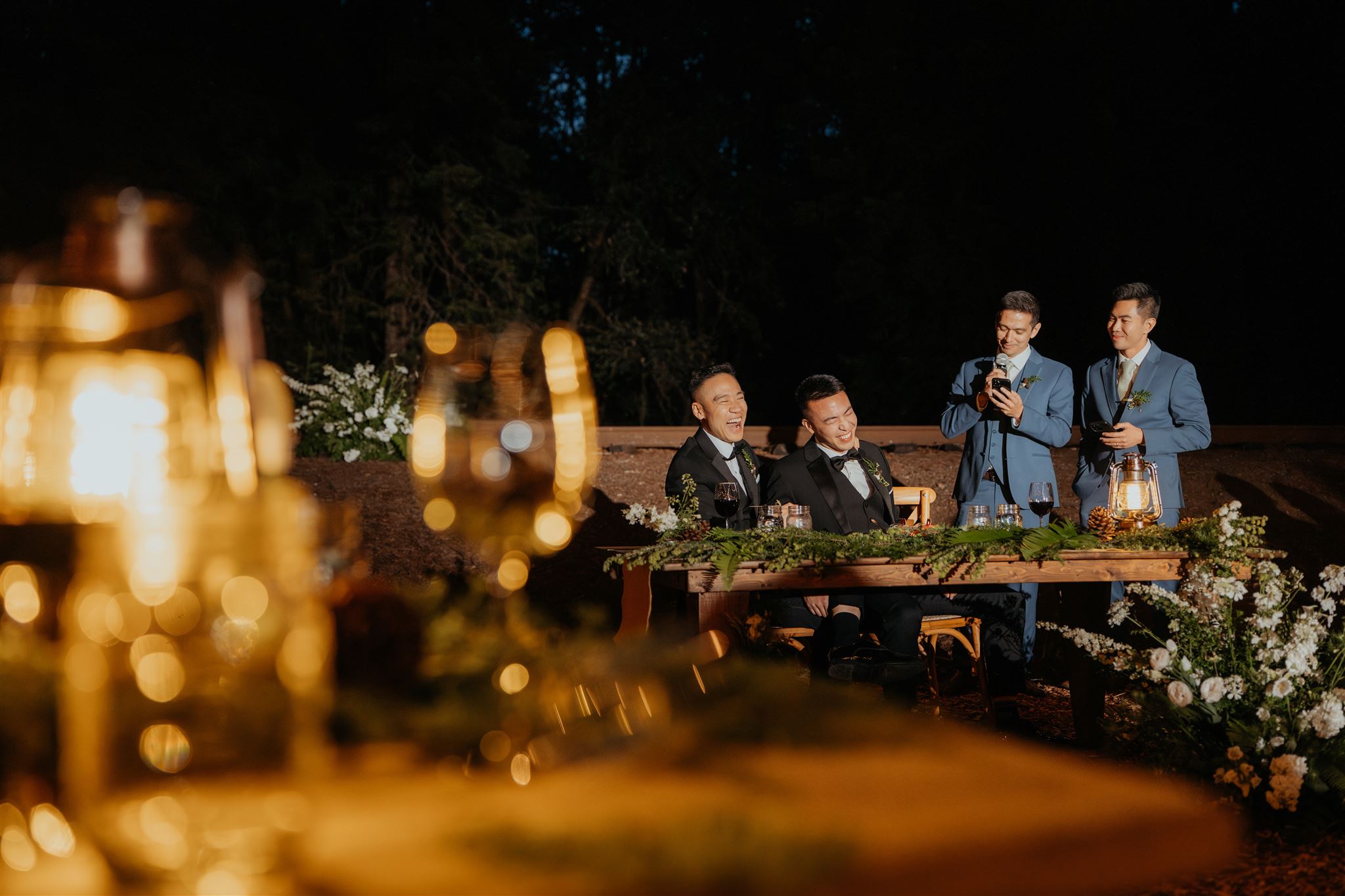 Grooms laugh while guests give speeches and toasts during their multi-day wedding reception dinner.