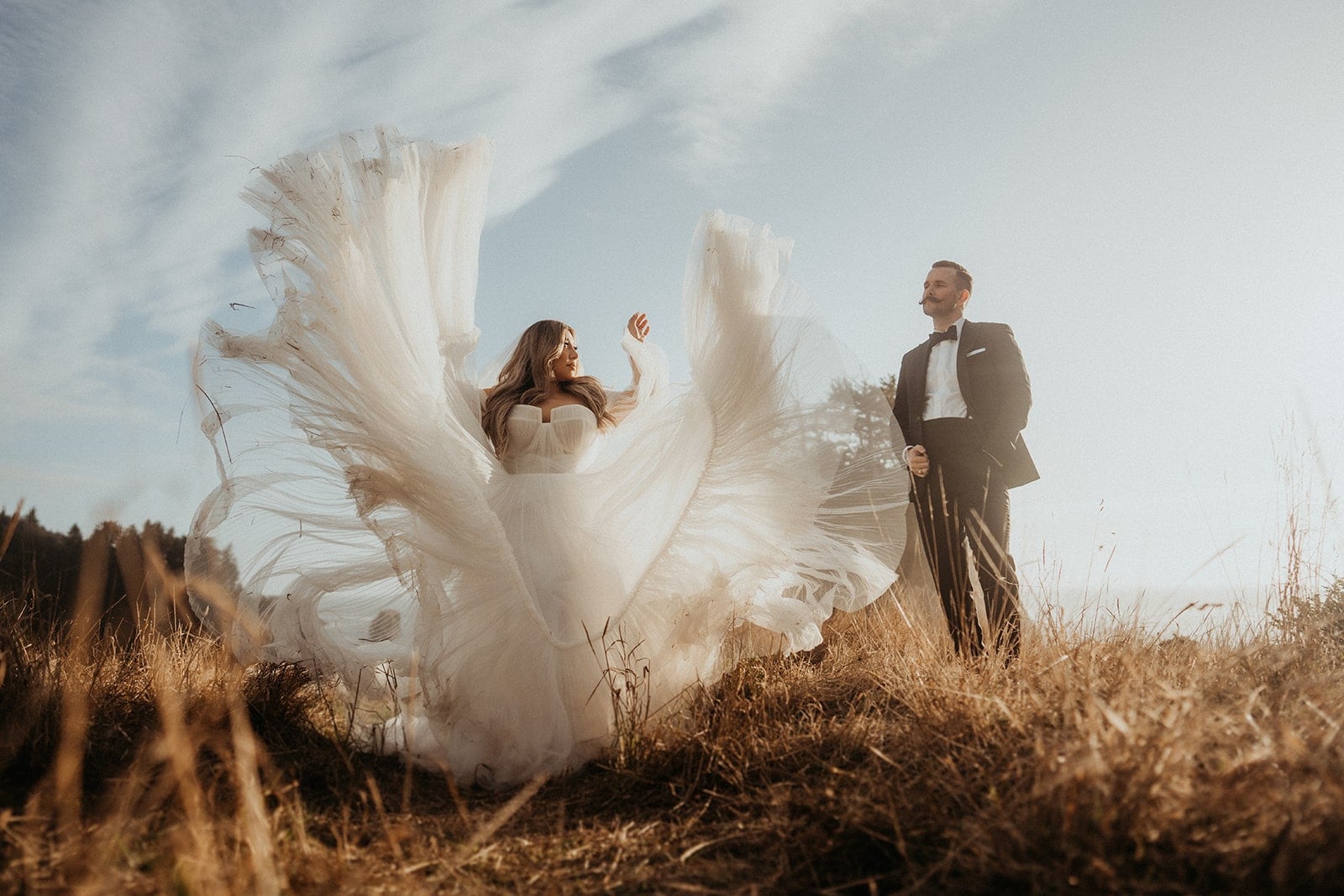 Bride flips her wedding dress in the air while groom looks on beside her during their Oregon Cost wedding weekend.