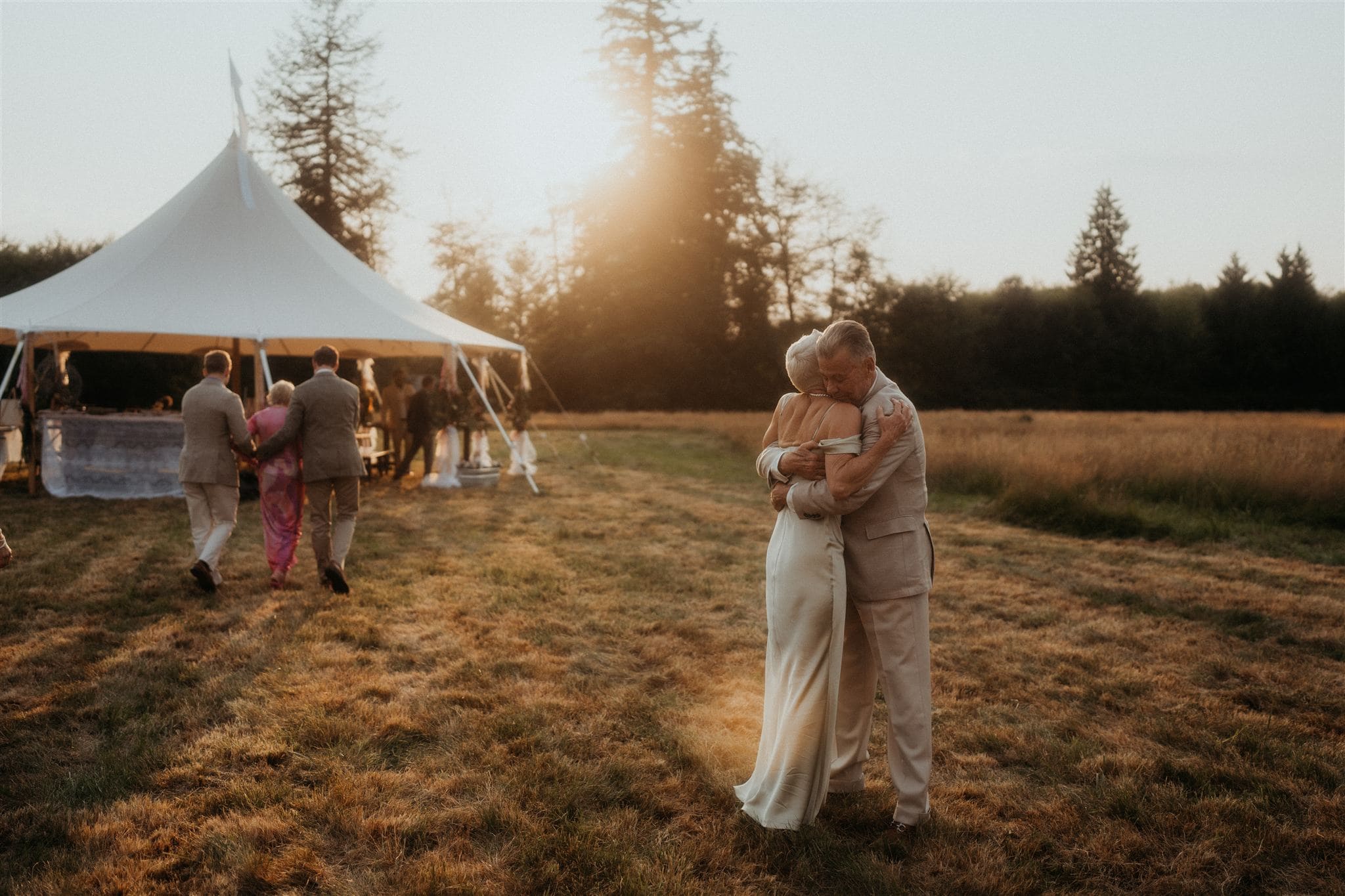 Parents of the bride hug beside a white backyard tent during their daughter's micro wedding in Washington.