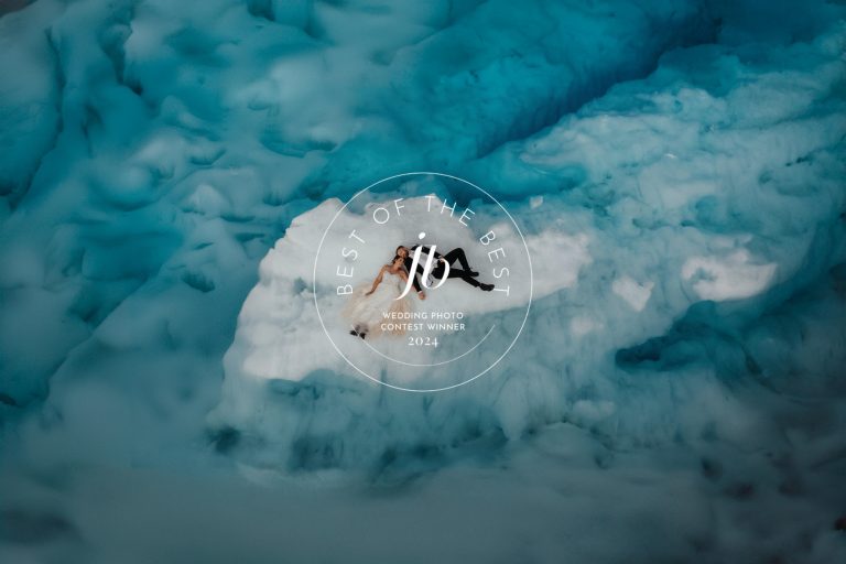 Bride and groom lay on a small island of ice surrounded by blue glacier water during their Alaska elopement.