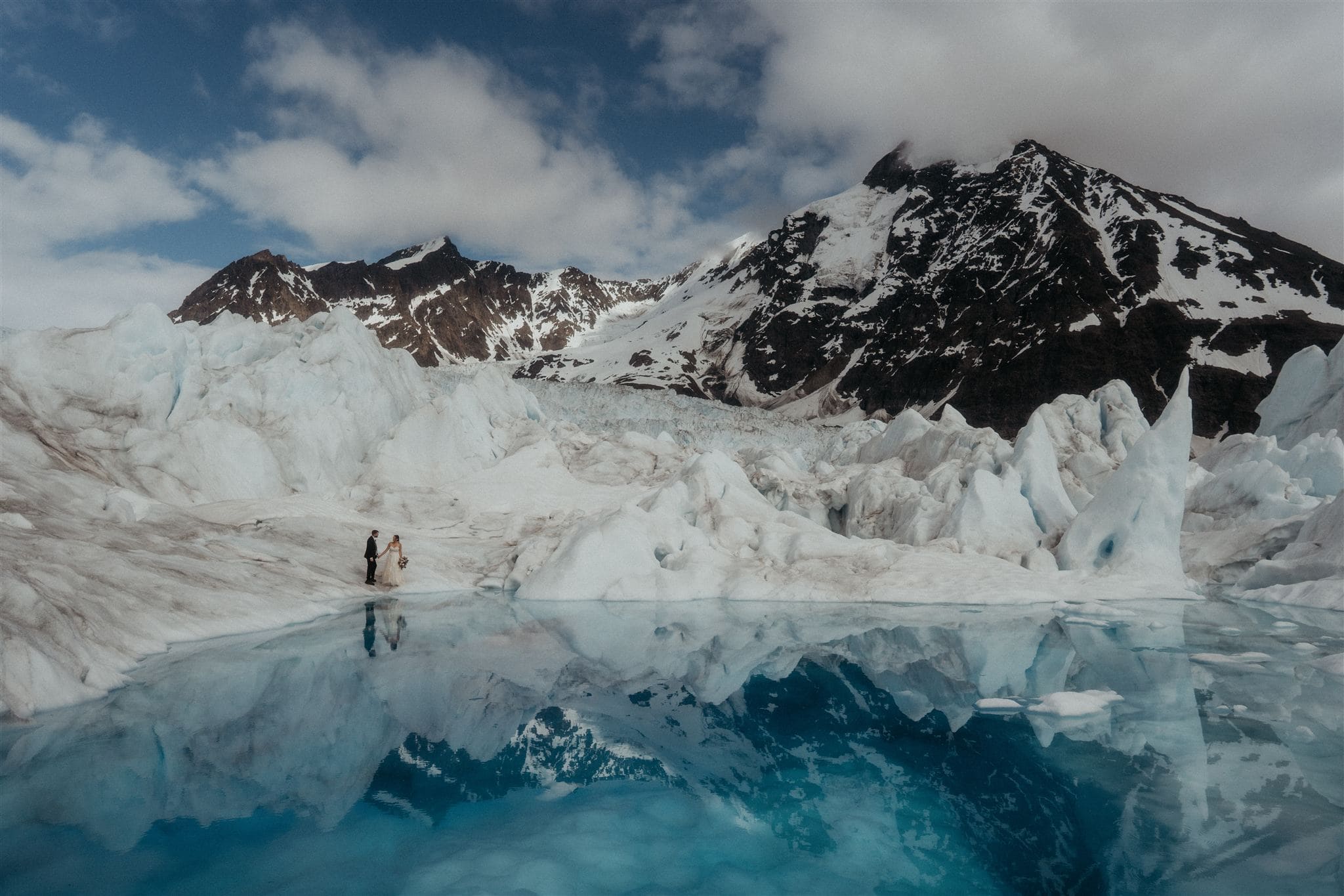 Bride and groom hold hands by an icy blue glacier lake during their Alaska elopement.