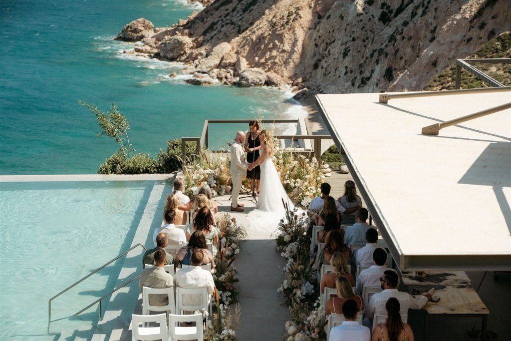 Bride and groom hold hands at their resort wedding ceremony during their destination wedding in Milos Greece.