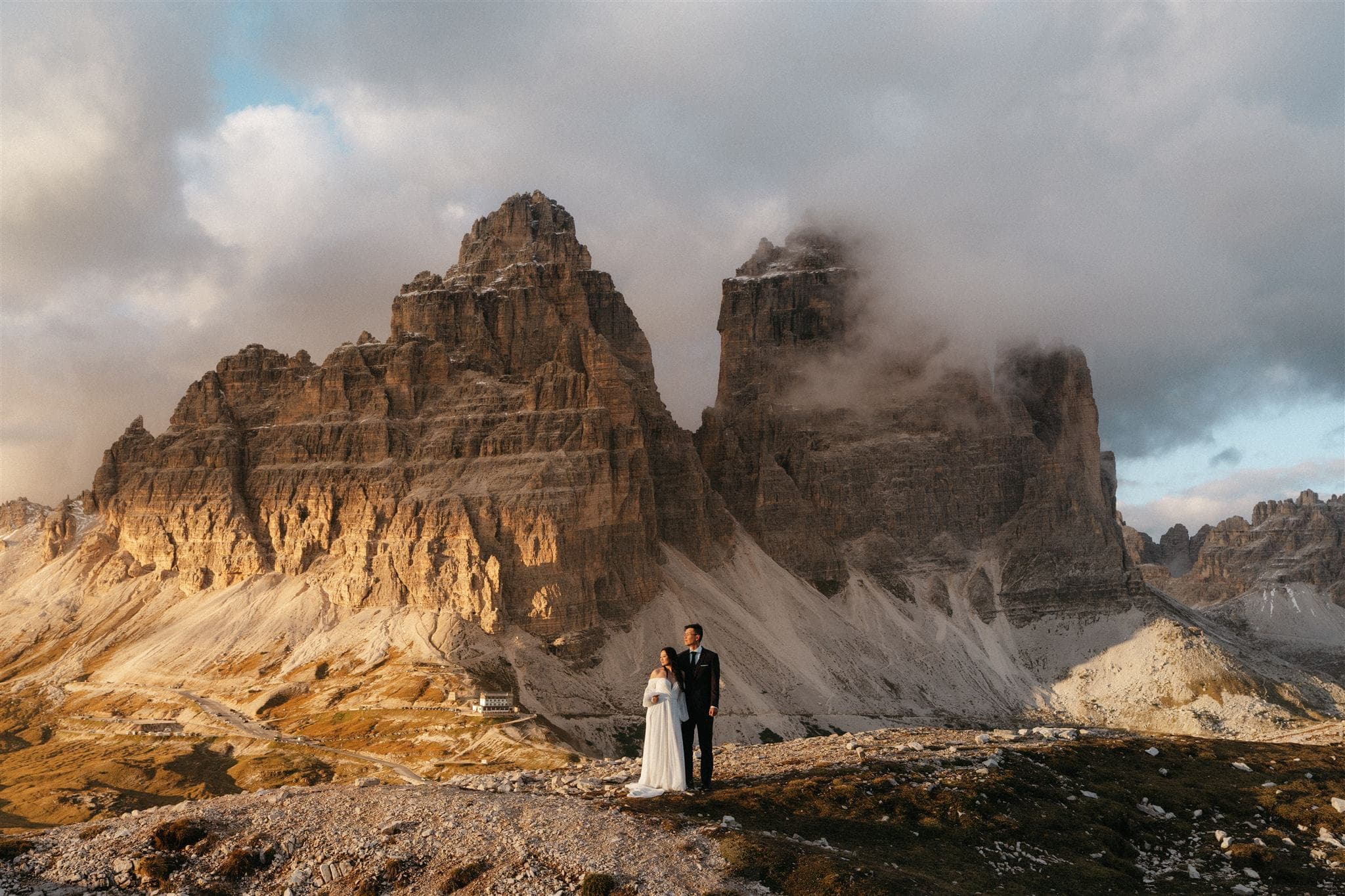Bride and groom stand on a mountain trail in the Dolomites during sunset.