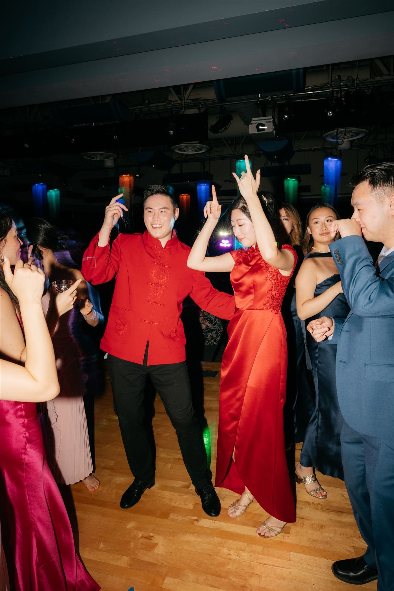 Bride and groom dance with their guests while wearing traditional Chinese wedding attire at their reception.