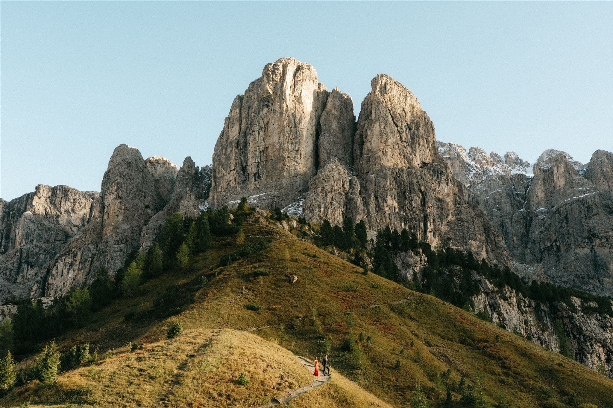 Bride and groom walk a mountain trail in the Dolomites while wearing their Chinese wedding attire.