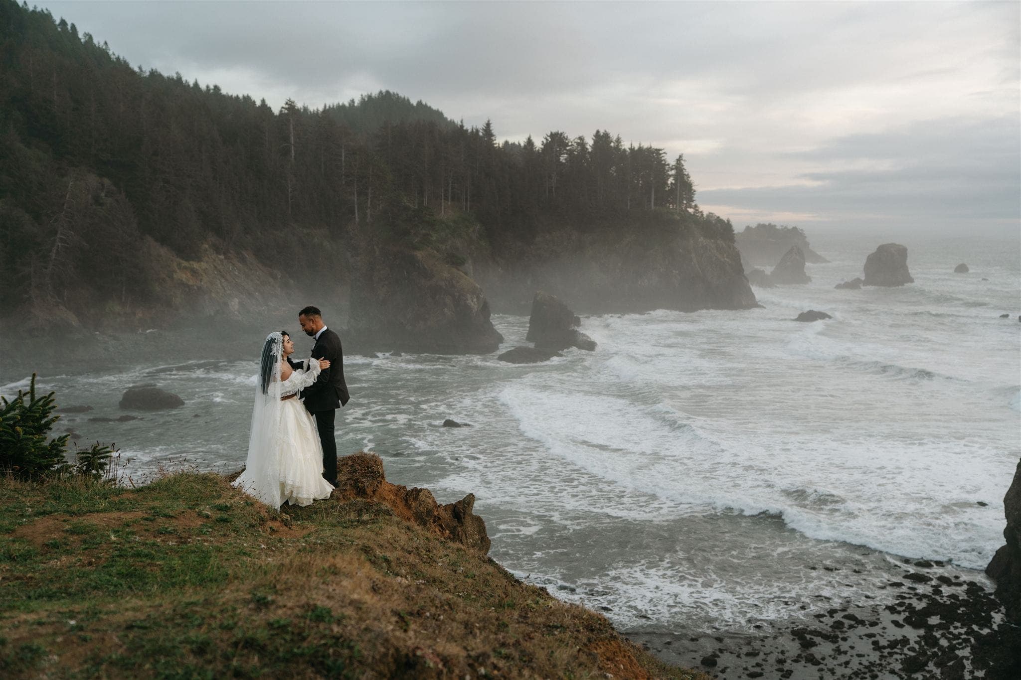 Bride and groom embrace on a misty Oregon cliff along the coast.