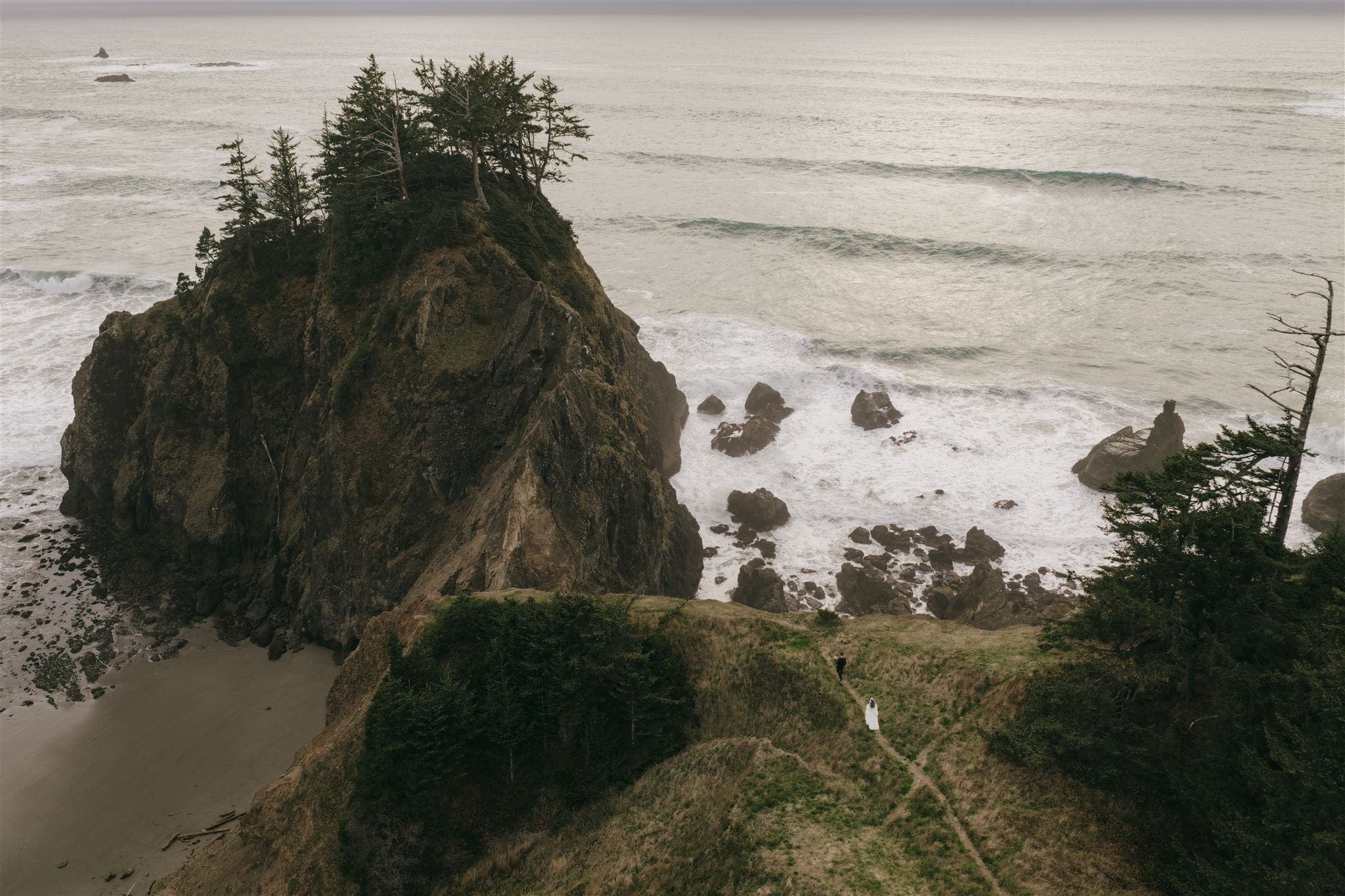 Bride and groom walk a grassy trail toward the Oregon Coast during their wedding portraits.