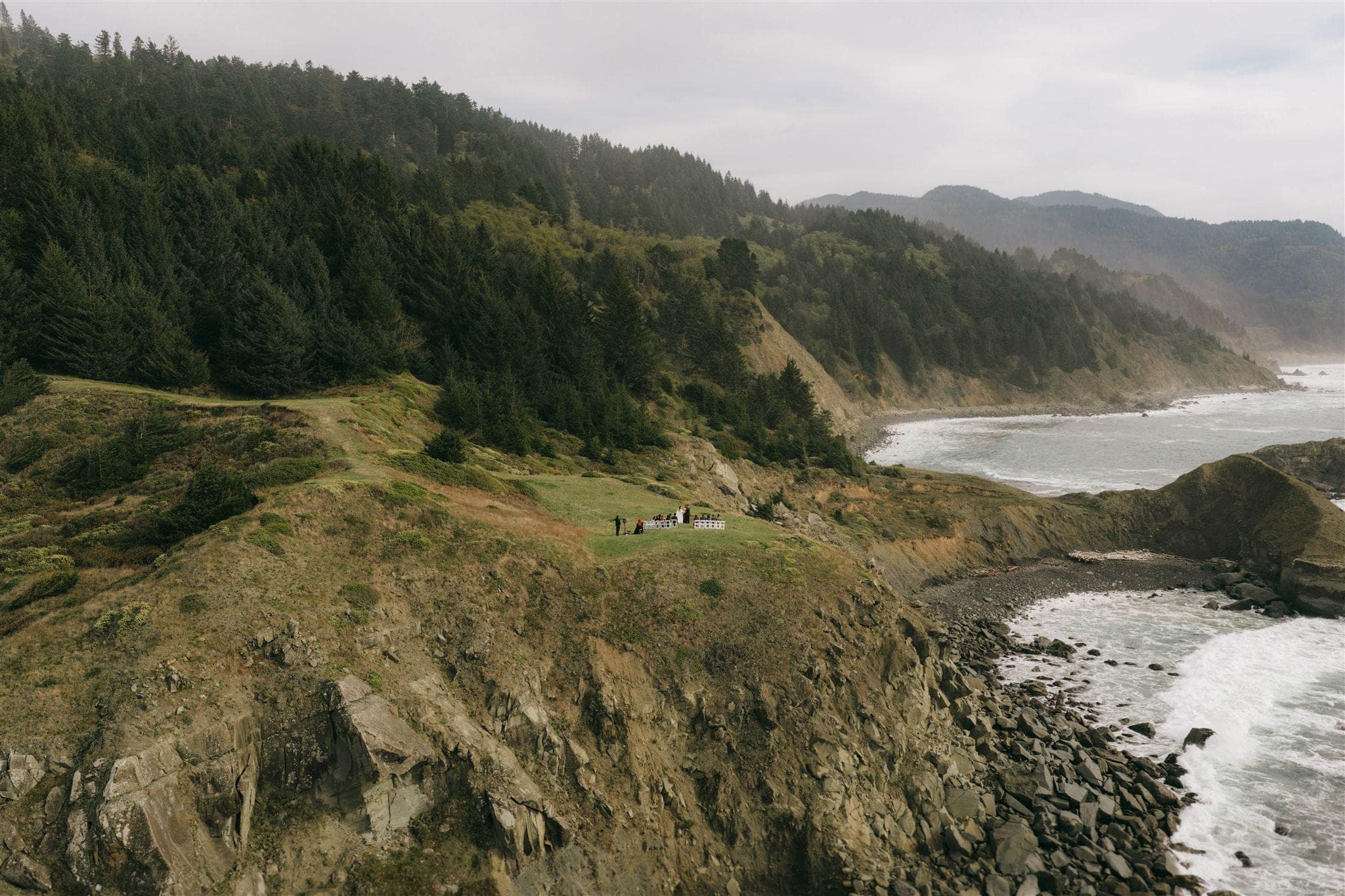Guests sit in white folding chairs during a Standstone Point Oregon wedding ceremony.