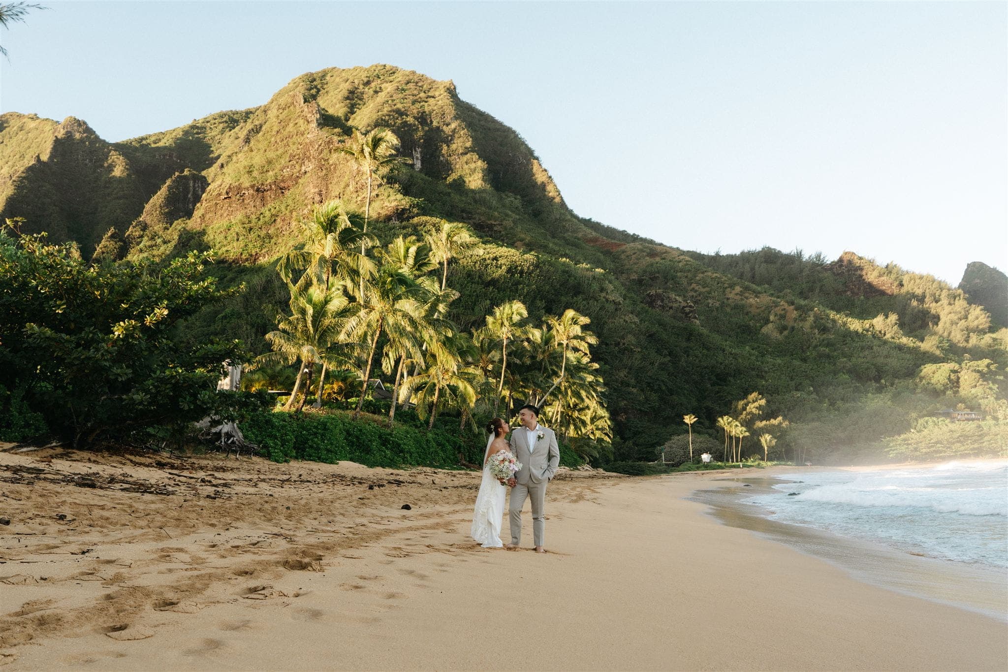 Bride and groom stand on a sandy beach during their Tunnels Beach elopement in Kauai.