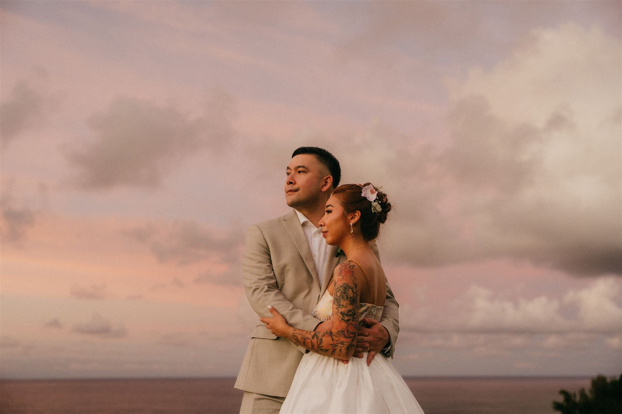 Bride and groom embrace while watching a pink Hawaii sunset during their luxury elopement in Kauai.