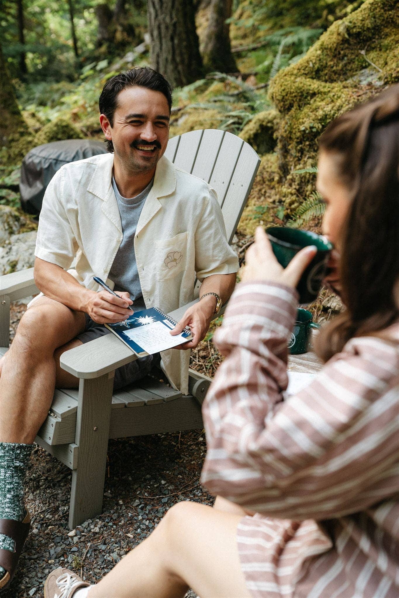 Couple sits on outdoor patio writing elopement letters while drinking coffee.