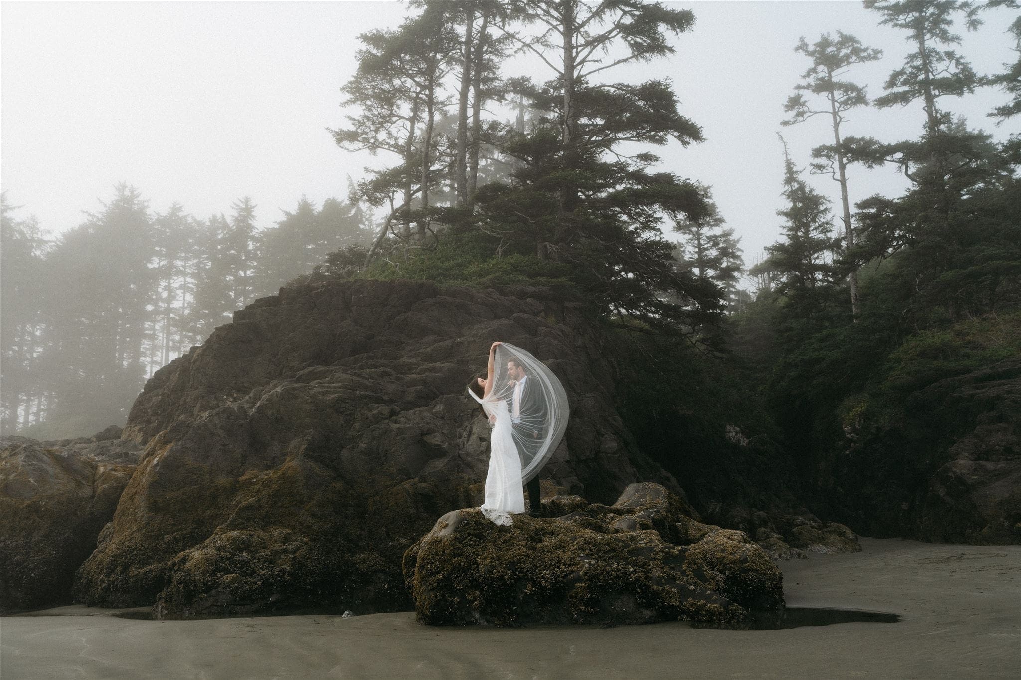 Newlyweds stand on a rock formation during their Tofino beach elopement.