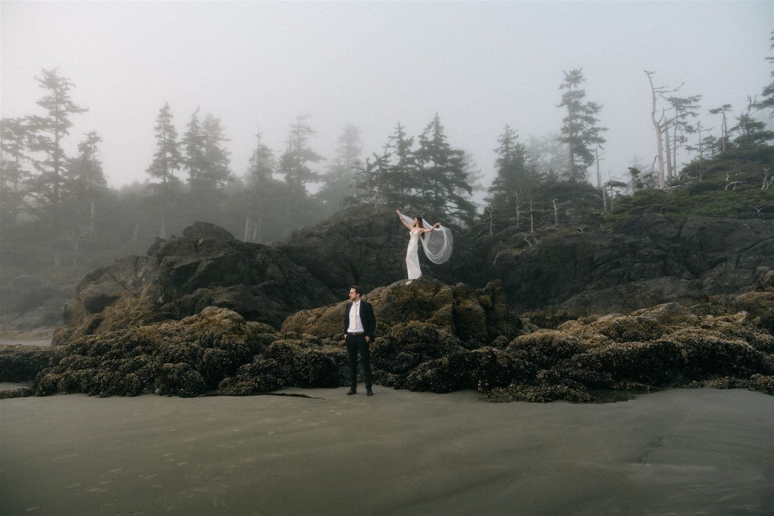 Newlyweds stand on a rock formation during their Tofino beach elopement.