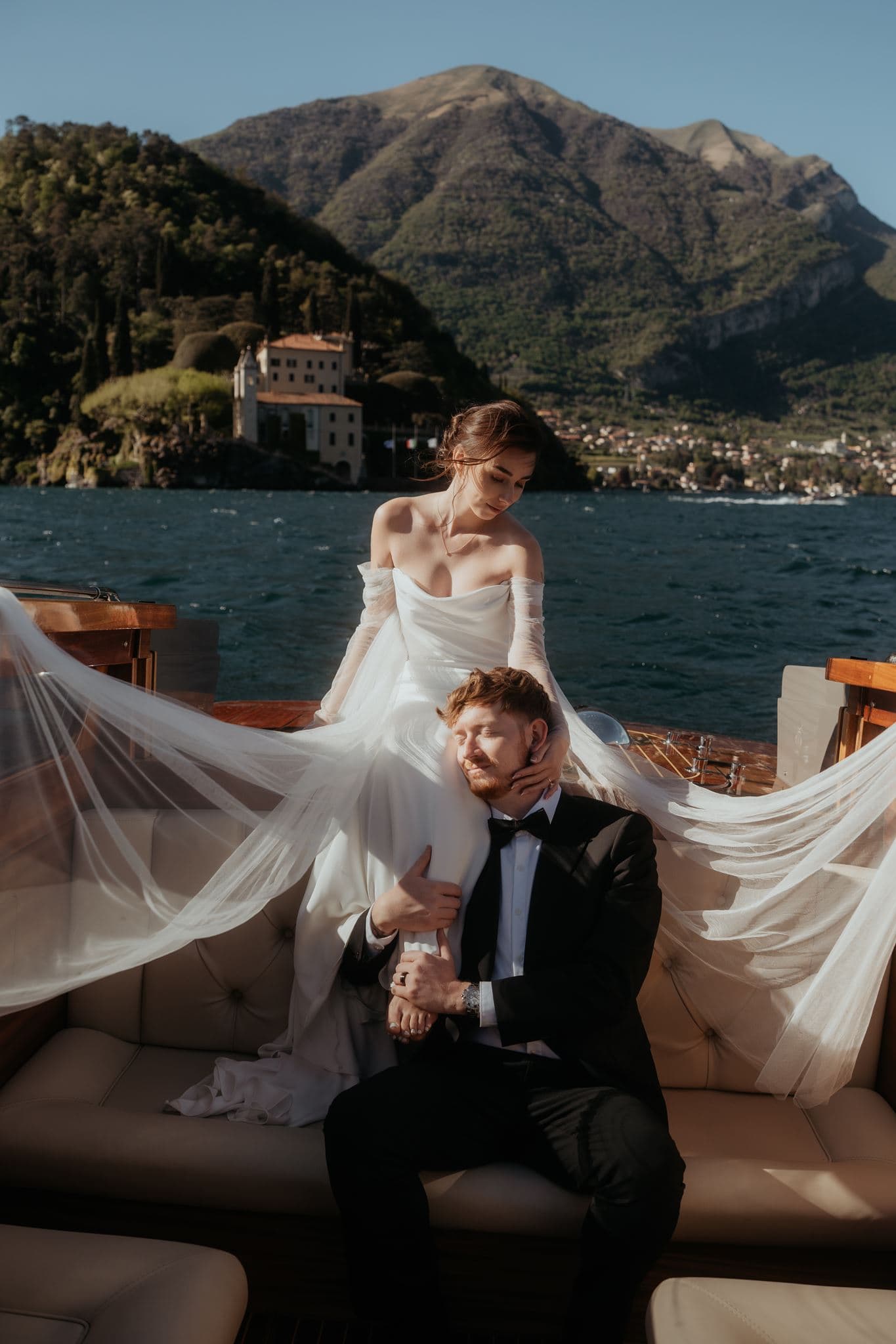Elegant wedding couple on a boat with scenic lake and mountain backdrop.