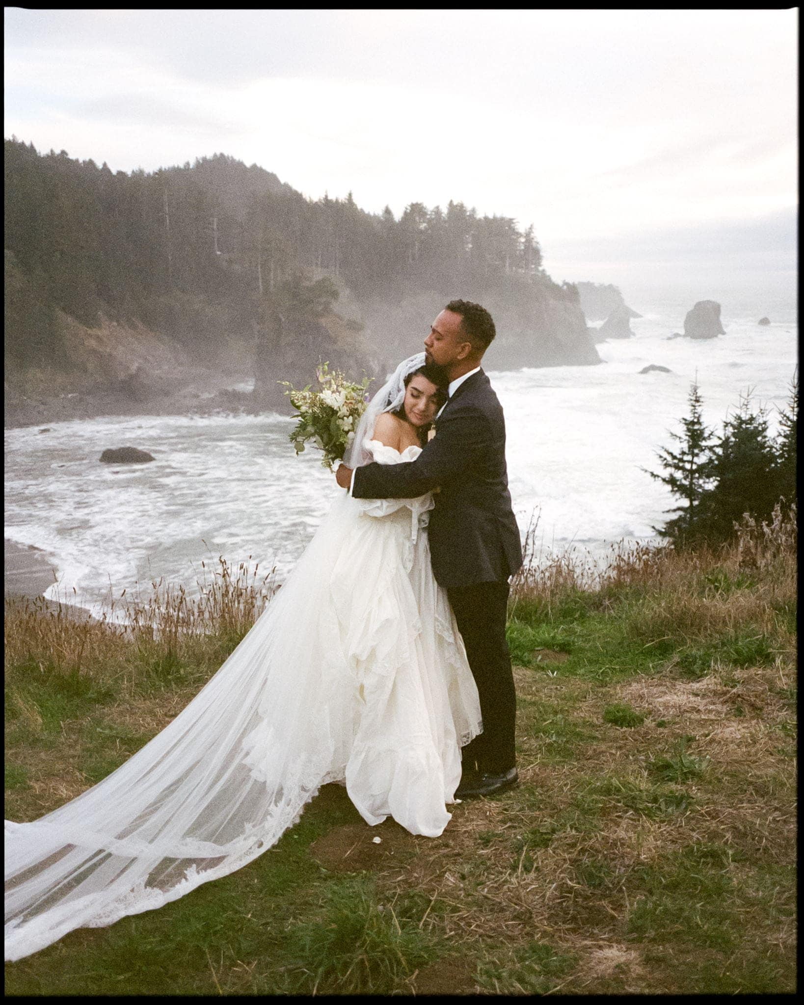 Bride and groom hug on a coastal cliff in Oregon during their film wedding photography portraits.