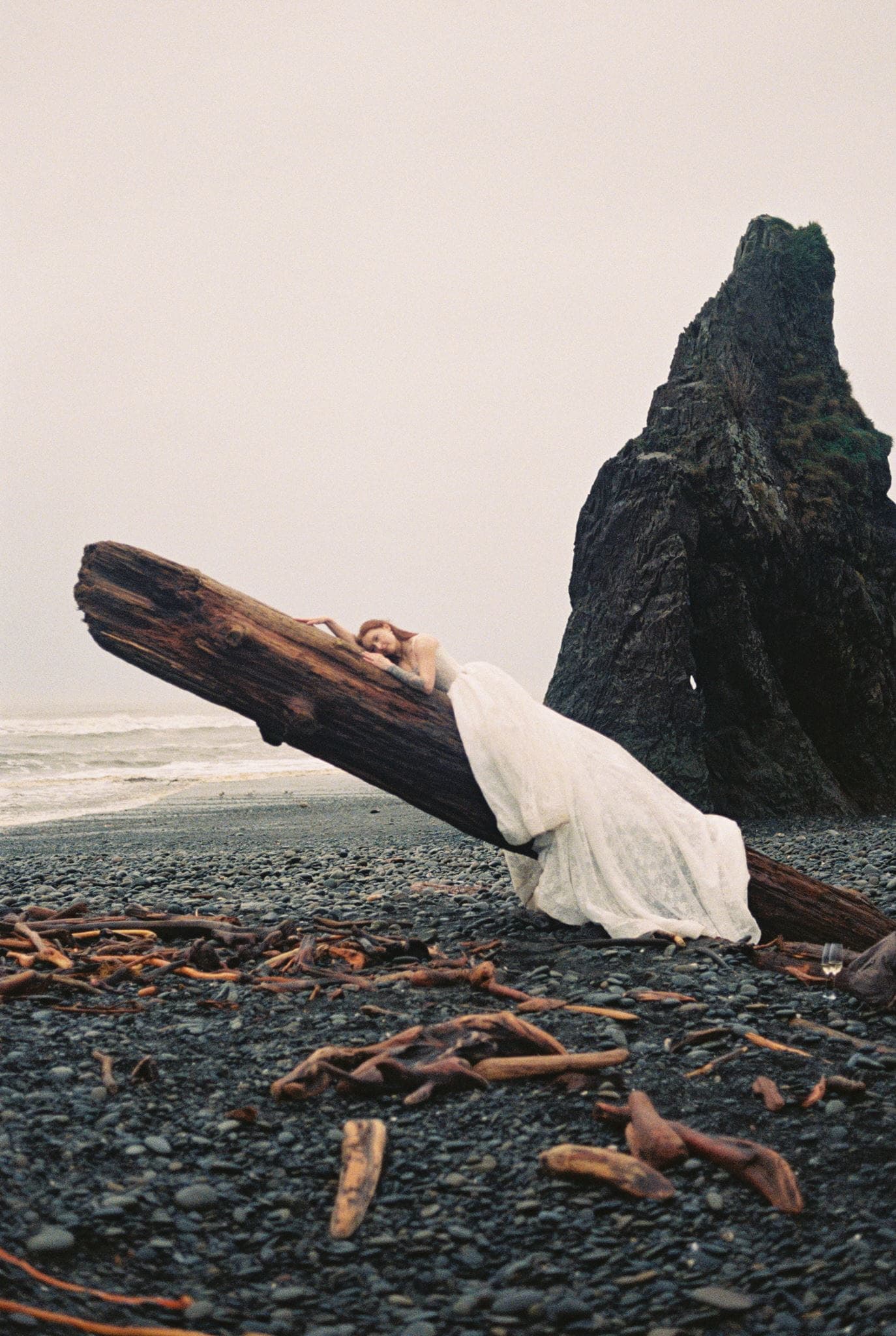 Bride lays down on a fallen tree on the coast during her film wedding portraits in Washington.
